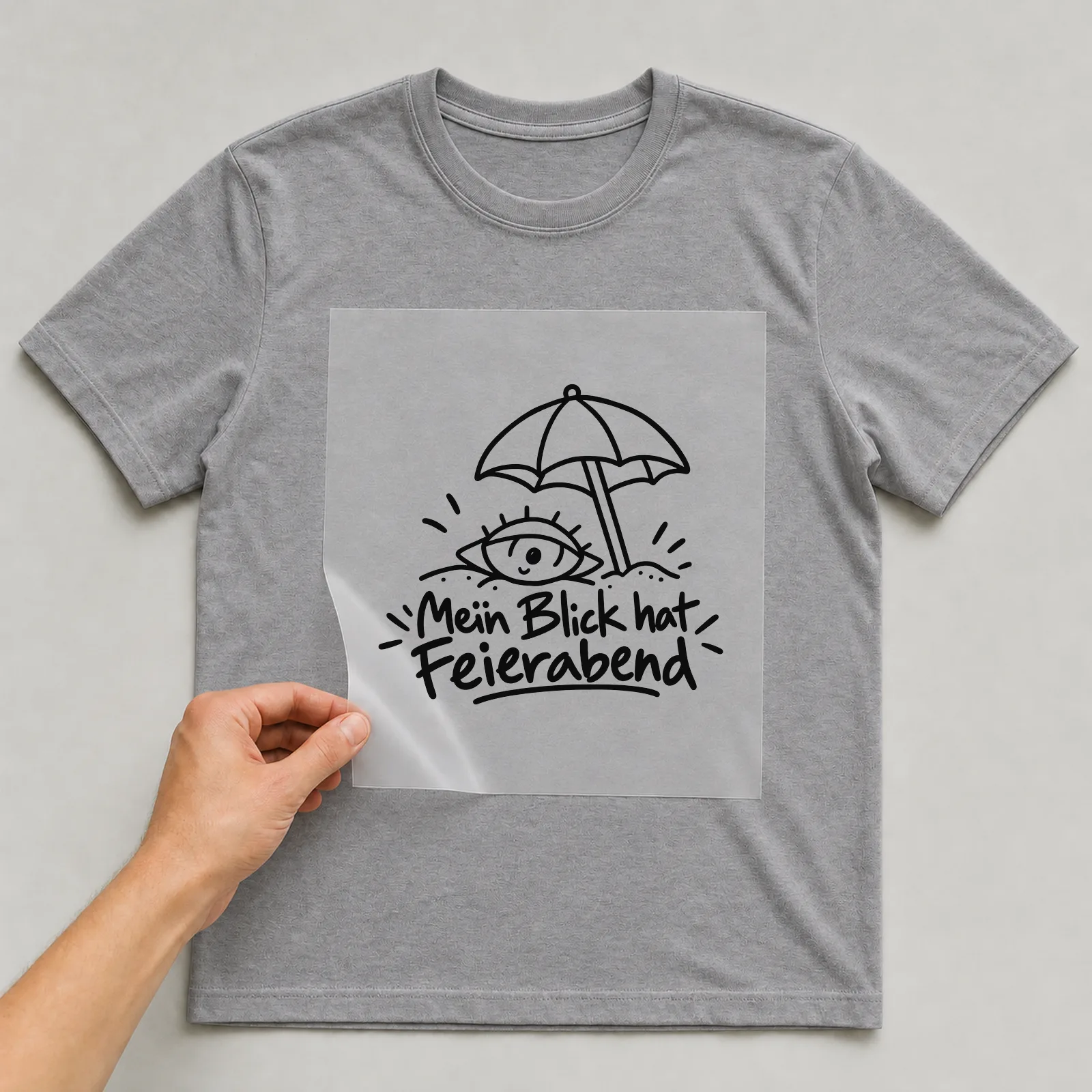Bügelbild „Mein Blick hat Feierabend“ auf grauem T-Shirt, Folie wird aufgelegt