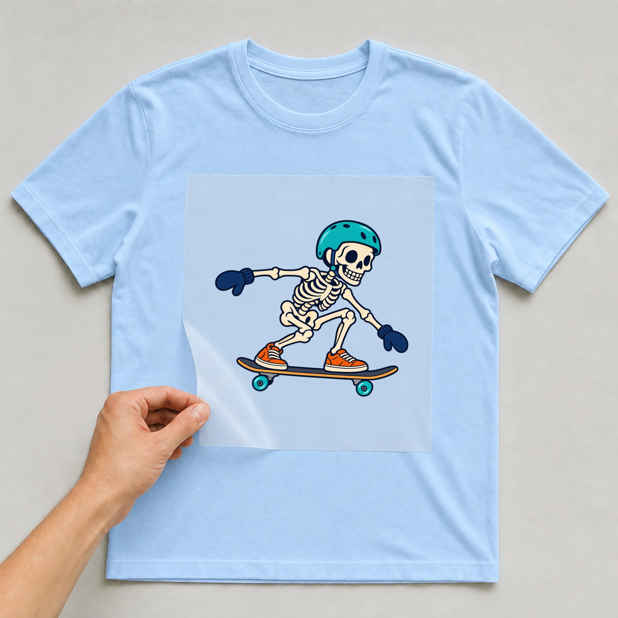 Bügelbild „Skeleton Skateboarding“ auf babyblauem T-Shirt, Folie wird aufgelegt