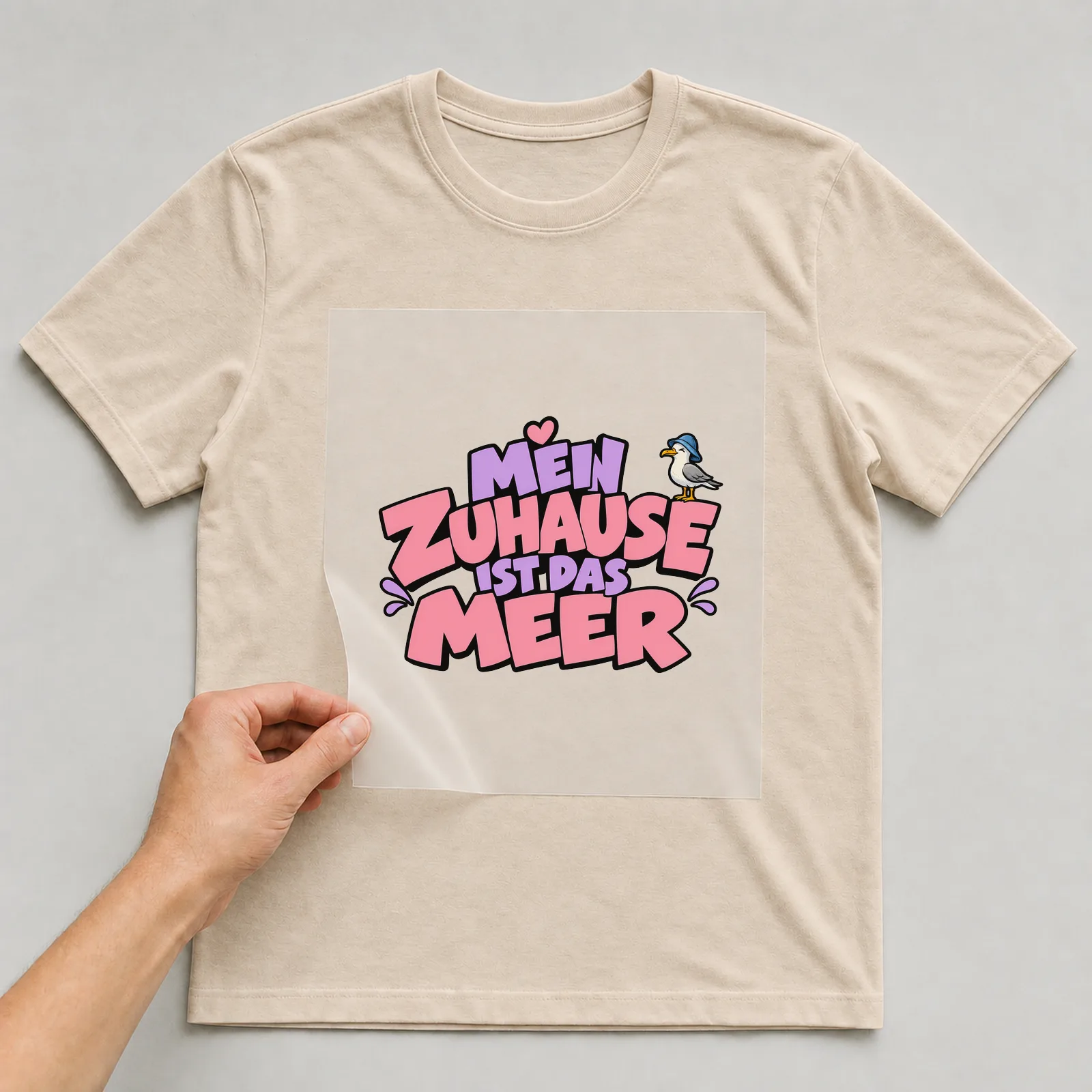 Bügelbild „Mein Zuhause ist das Meer“ auf beigem T-Shirt, Folie wird aufgelegt