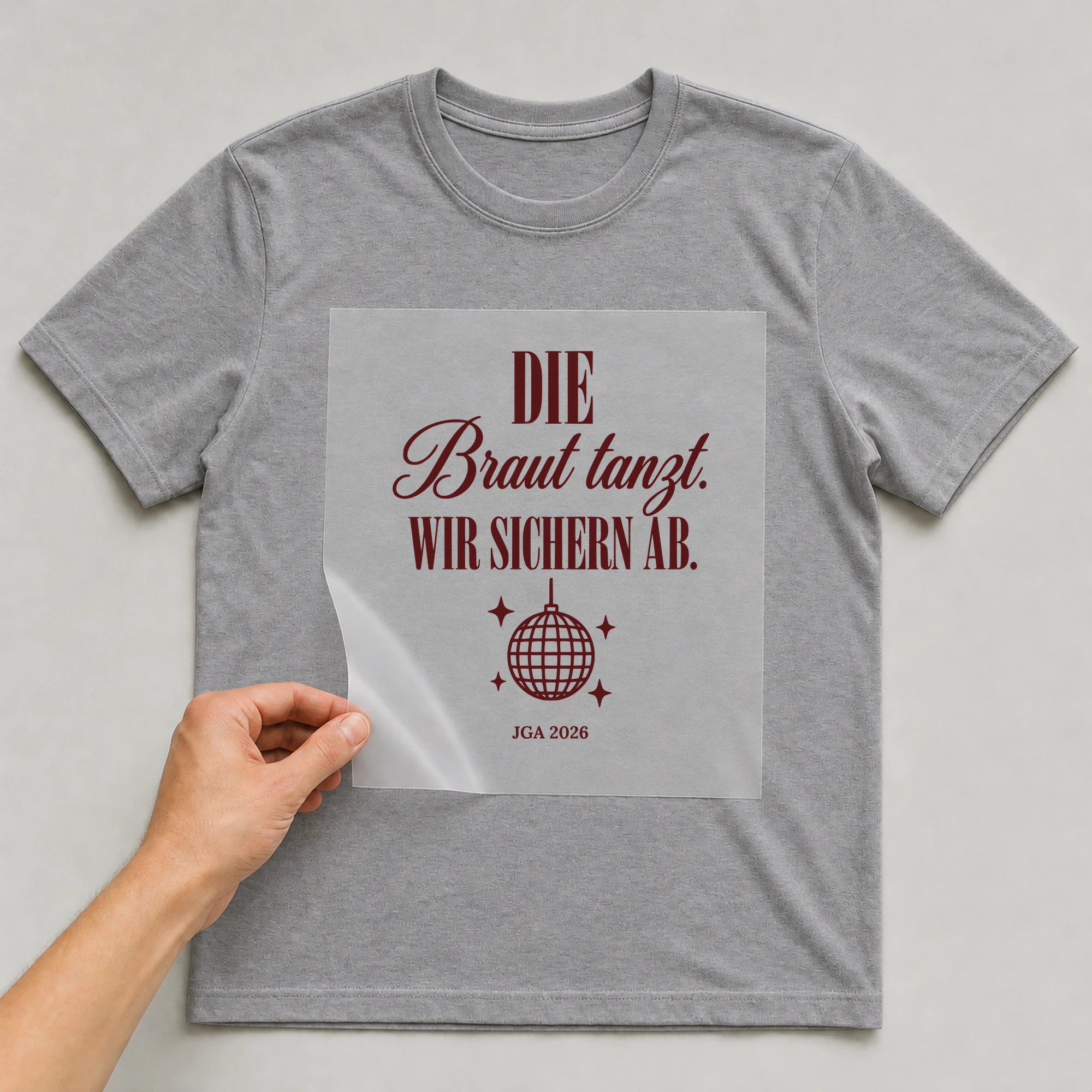 Bügelbild Die Braut tanzt. Wir sichern ab. auf grauem T-Shirt, Folie wird aufgelegt