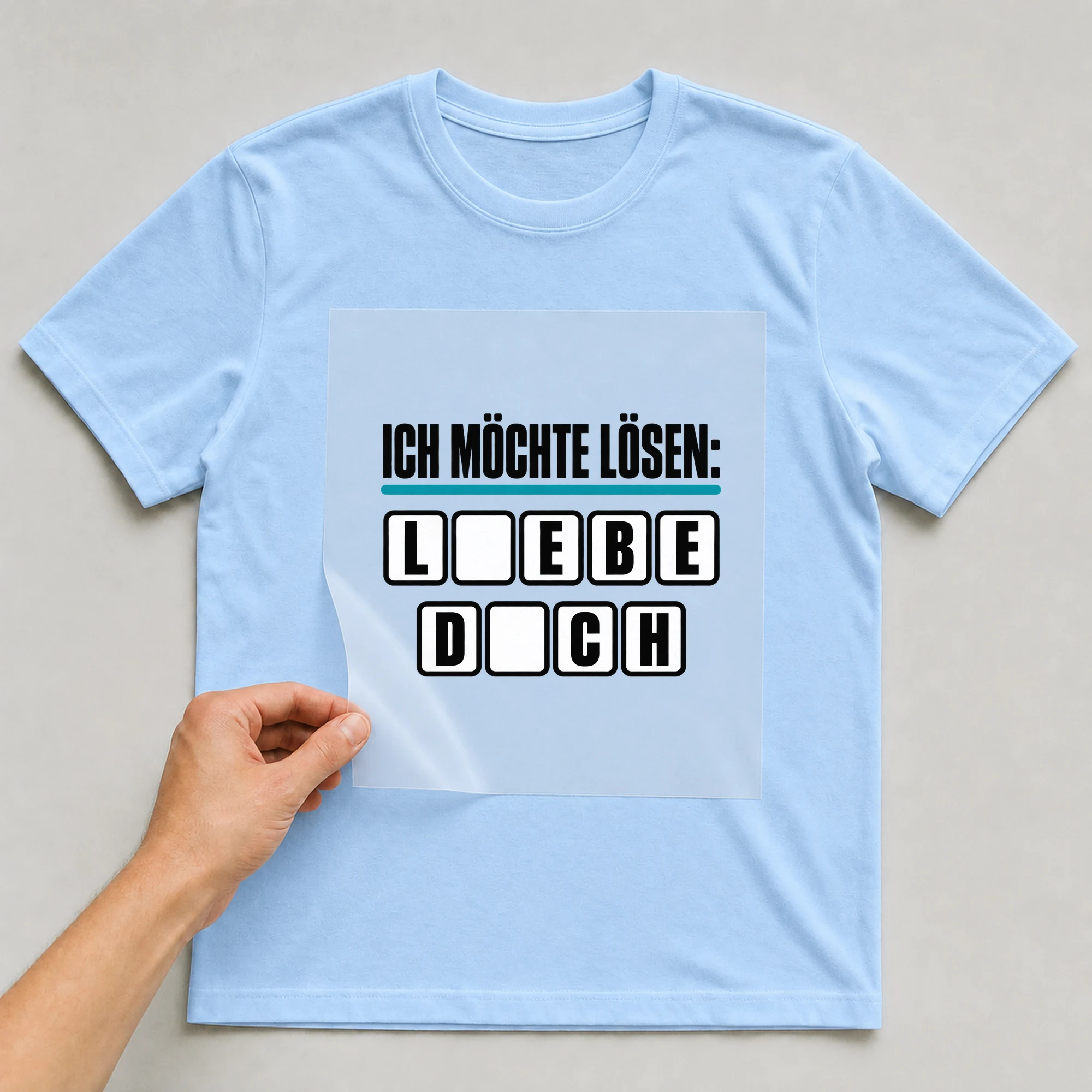 Bügelbild „Ich möchte lösen: Liebe dich“ auf babyblauem T-Shirt, Folie wird aufgelegt