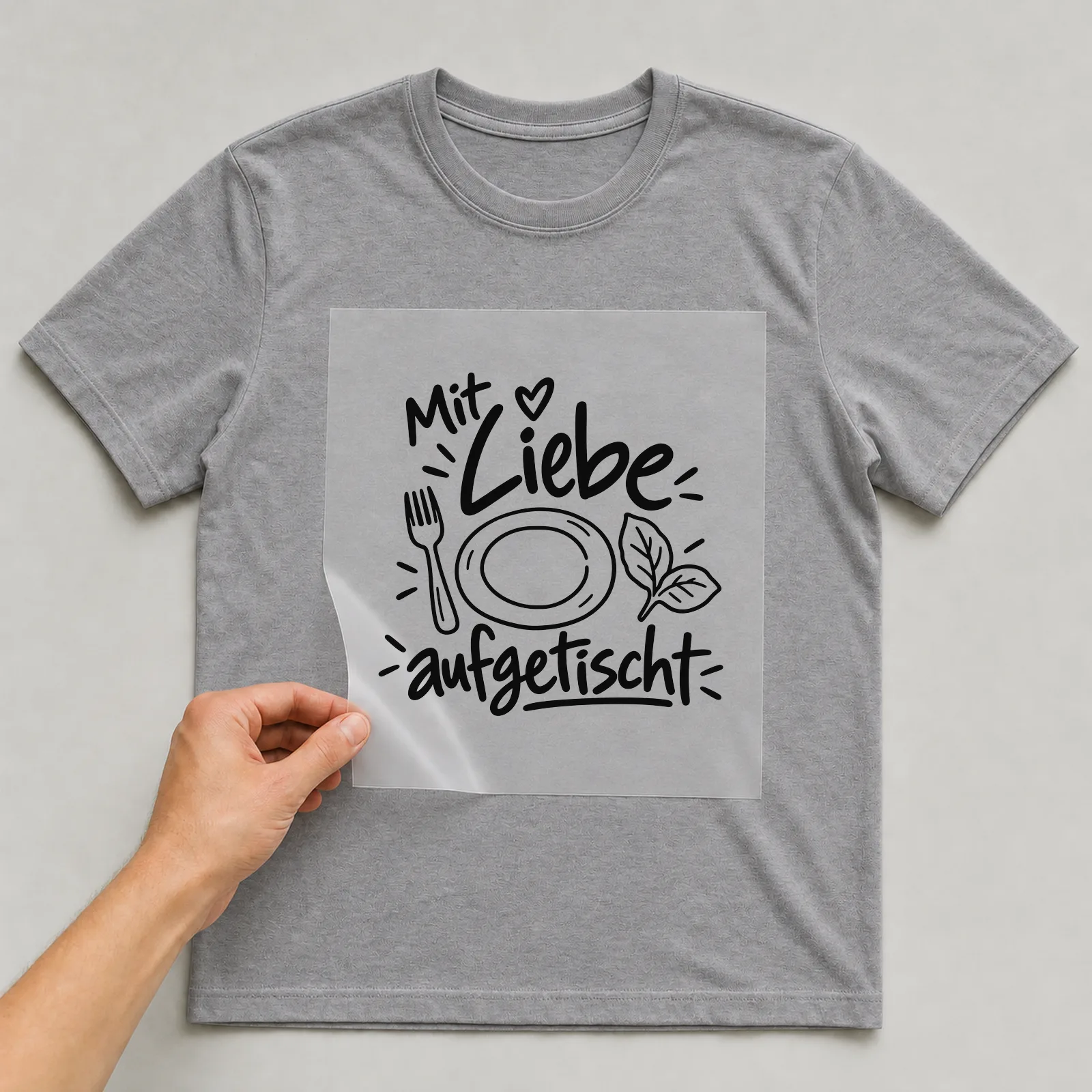 Bügelbild „Mit Liebe aufgetischt“ auf grauem T-Shirt, Folie wird aufgelegt