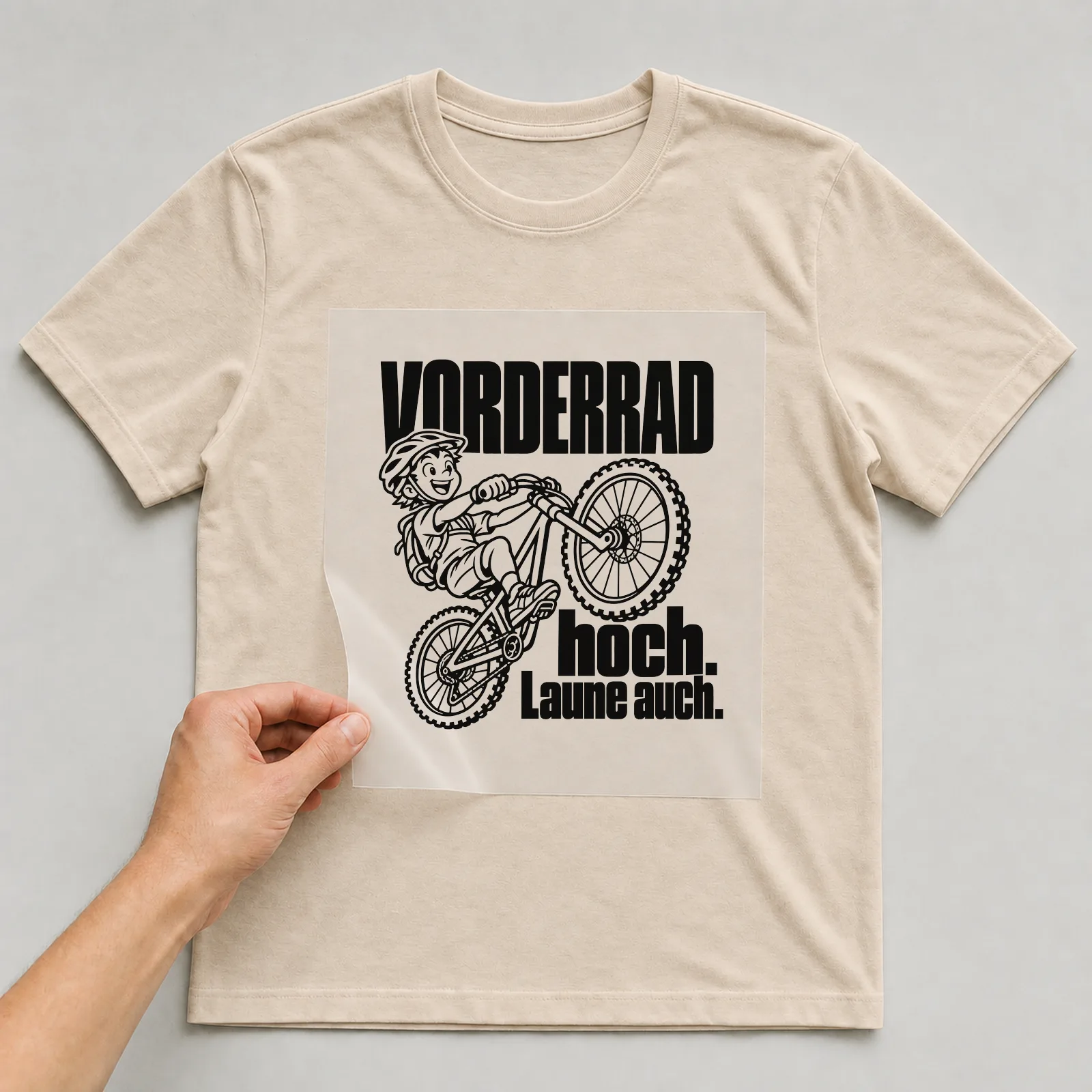 Bügelbild „Vorderrad hoch. Laune auch.“ auf beigem T-Shirt, Folie wird aufgelegt