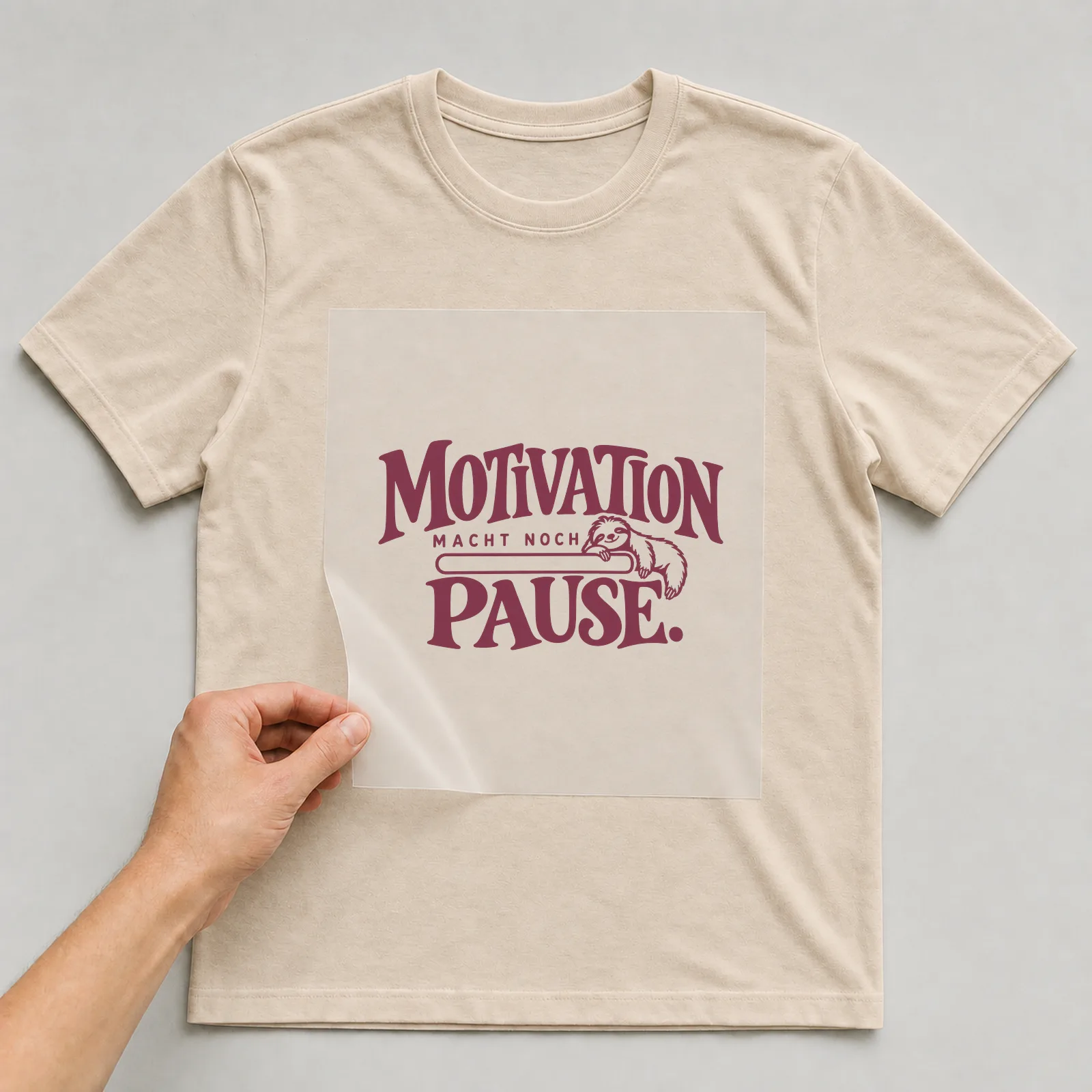 Bügelbild „Motivation macht noch Pause“ auf beigem T-Shirt, Folie wird aufgelegt