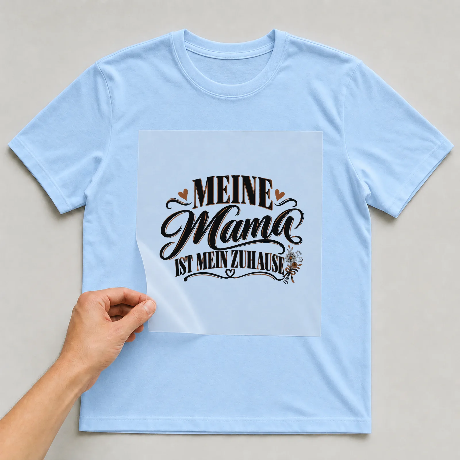 Bügelbild „Meine Mama ist mein Zuhause“ auf hellblauem T-Shirt, Folie wird aufgelegt