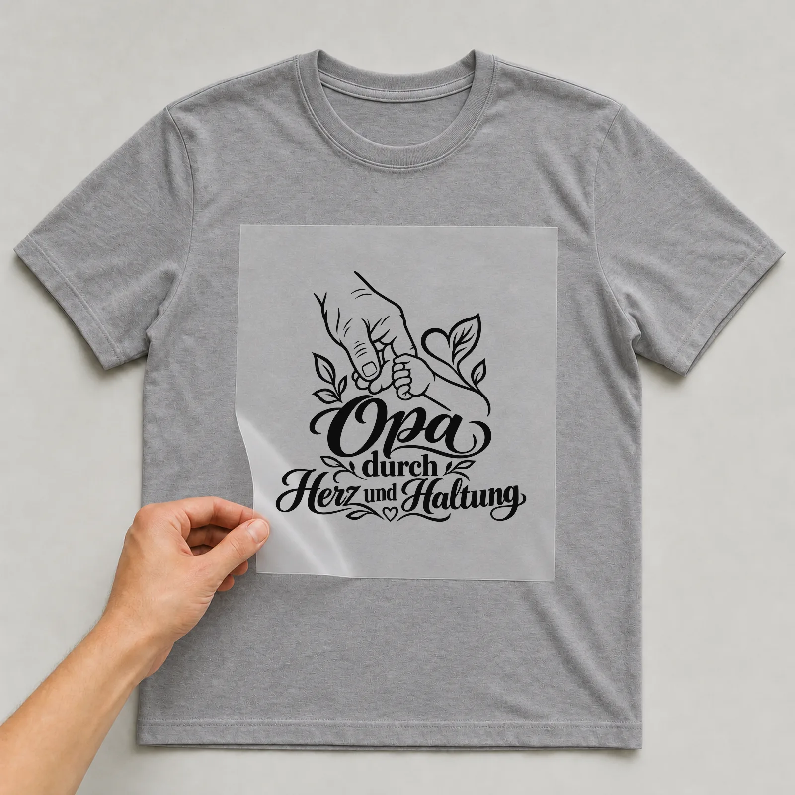 Bügelbild „Opa durch Herz und Haltung“ auf grauem T-Shirt, Folie wird aufgelegt