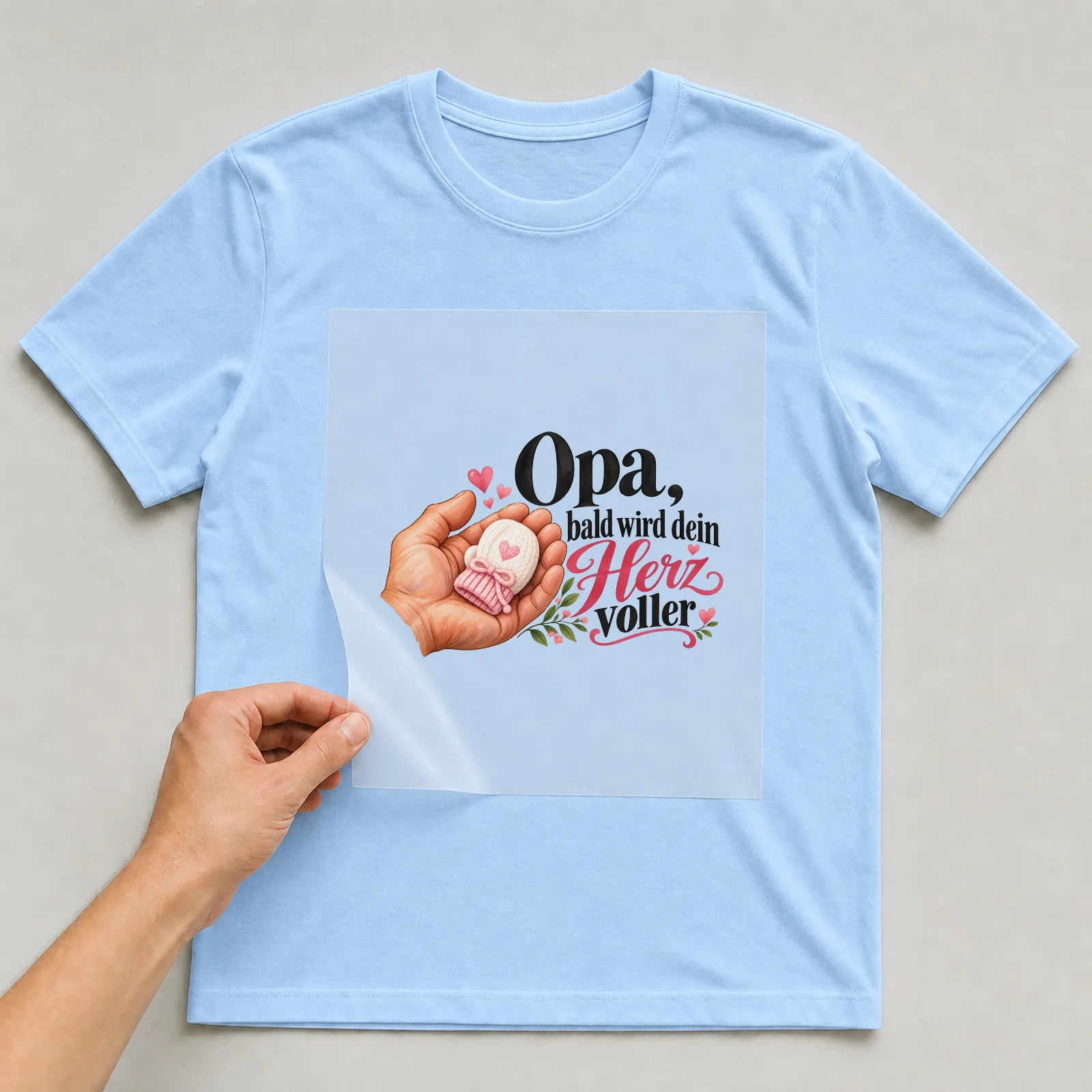 Bügelbild „Opa, bald wird dein Herz voller“ auf hellblauem T-Shirt, Folie wird aufgelegt
