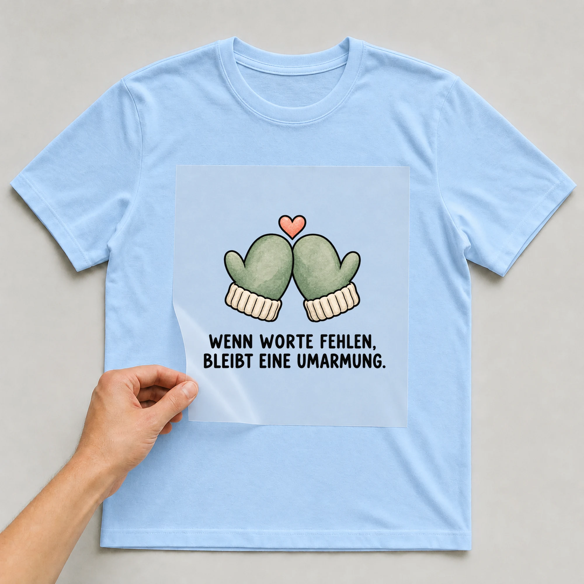 Bügelbild „WENN WORTE FEHLEN, BLEIBT EINE UMARMUNG.“ auf babyblauem T-Shirt, Folie wird aufgelegt