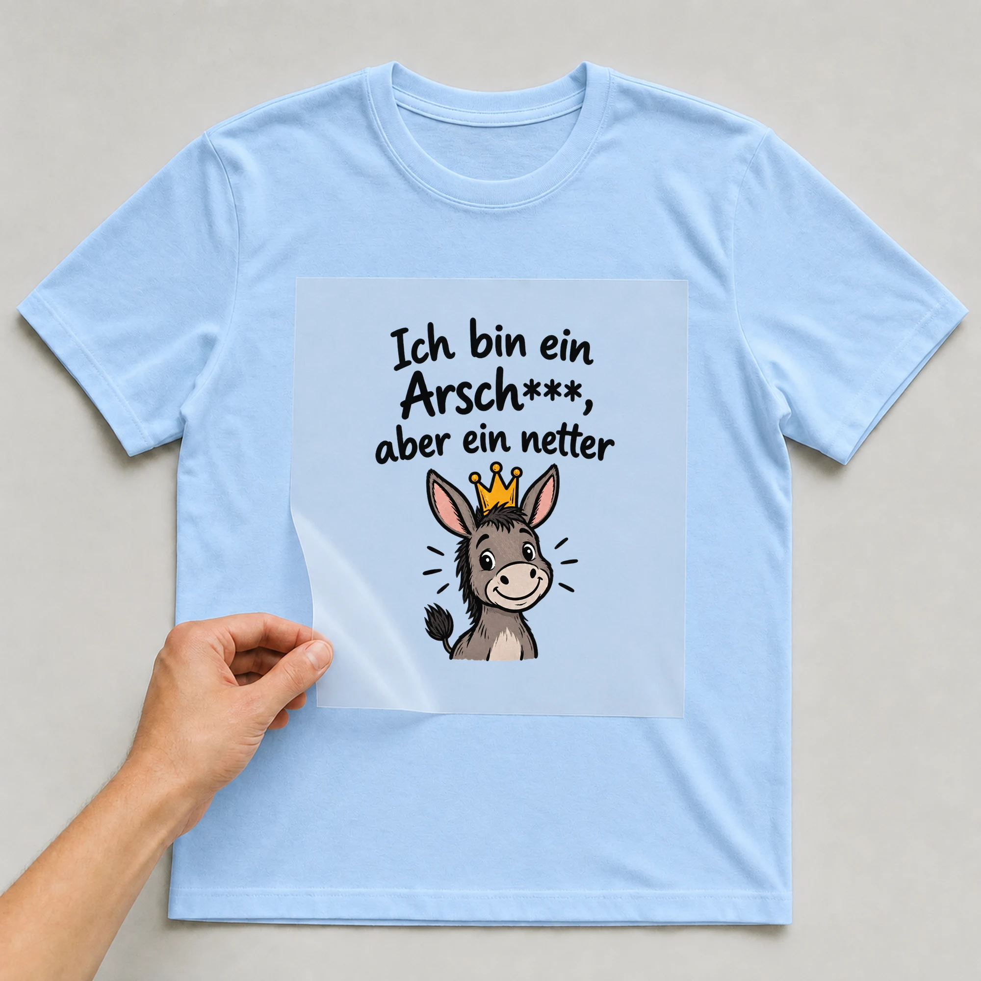 Bügelbild „Ich bin ein Arsch***, aber ein netter“ auf babyblauem T-Shirt, Folie wird aufgelegt