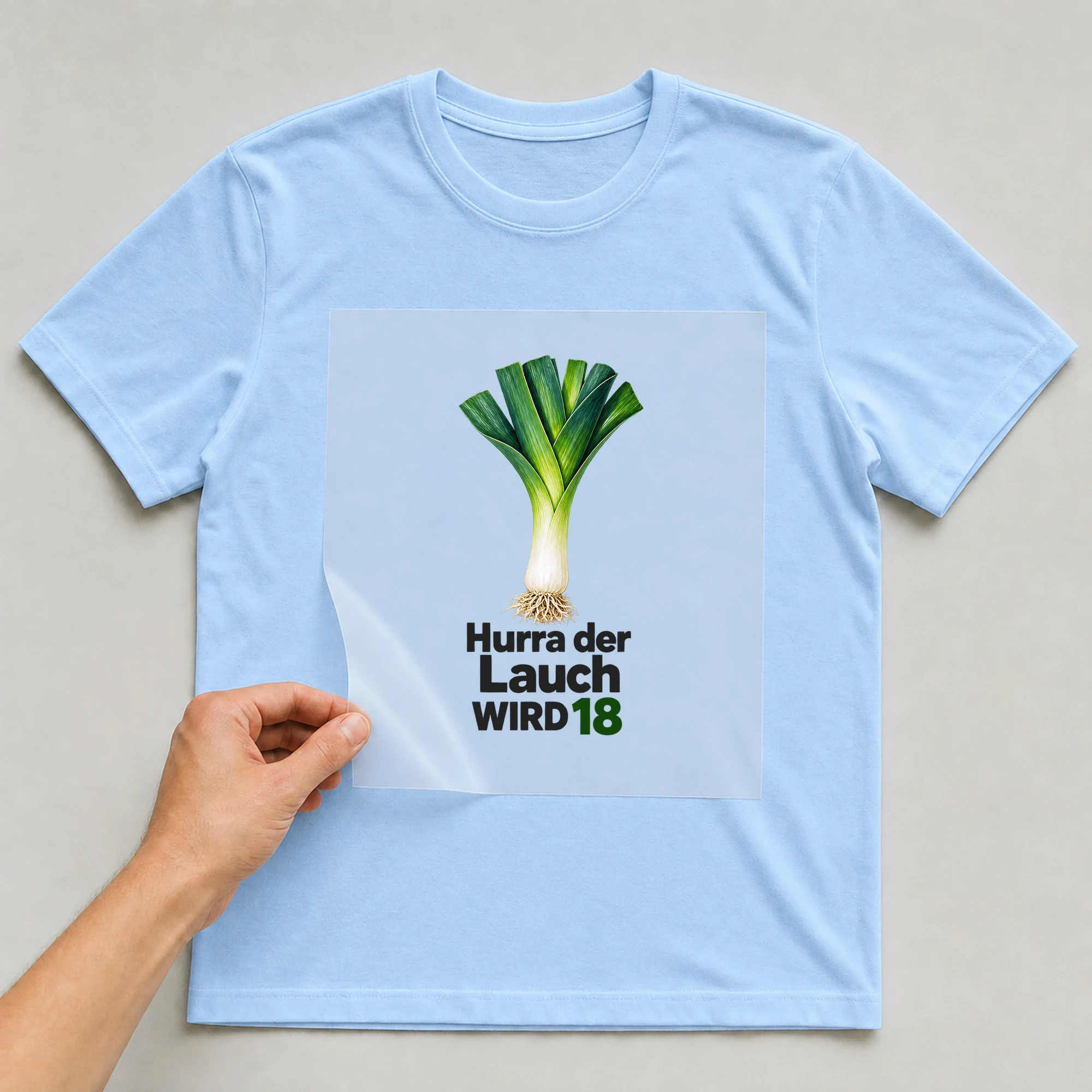 Bügelbild „Hurra der Lauch WIRD 18“ auf babyblauem T-Shirt, Folie wird aufgelegt