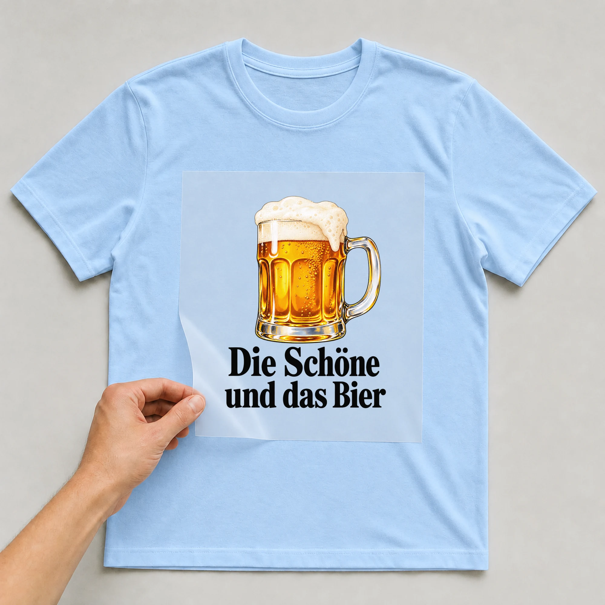 Bügelbild „Die Schöne und das Bier“ auf babyblauem T-Shirt, Folie wird aufgelegt