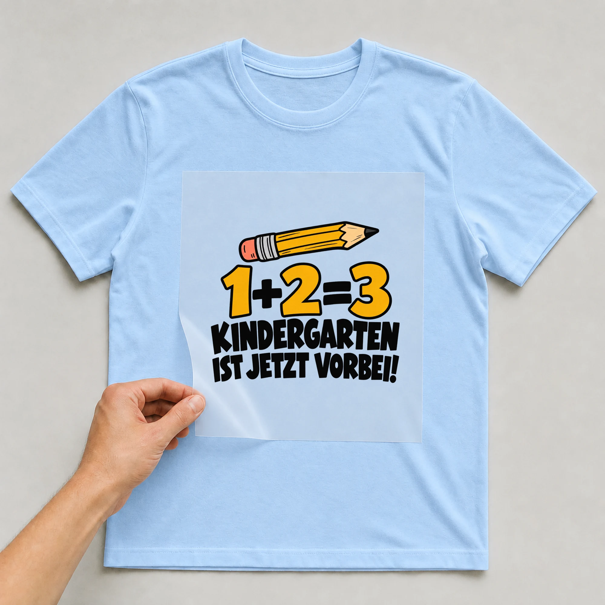 Bügelbild „1+2=3 Kindergarten ist jetzt vorbei!“ auf babyblauem T-Shirt, Folie wird aufgelegt