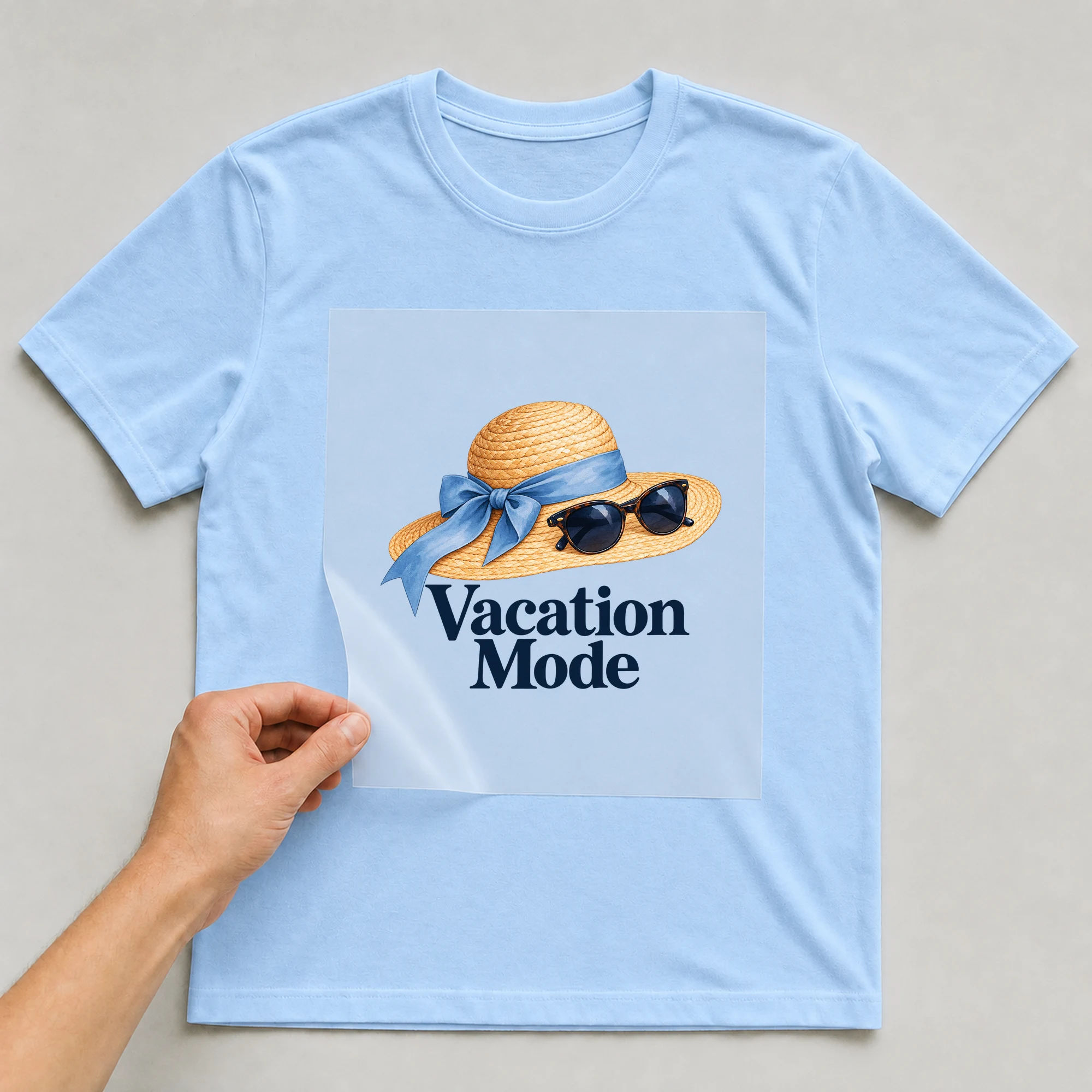 Bügelbild „Vacation Mode“ auf babyblauem T-Shirt, Folie wird aufgelegt