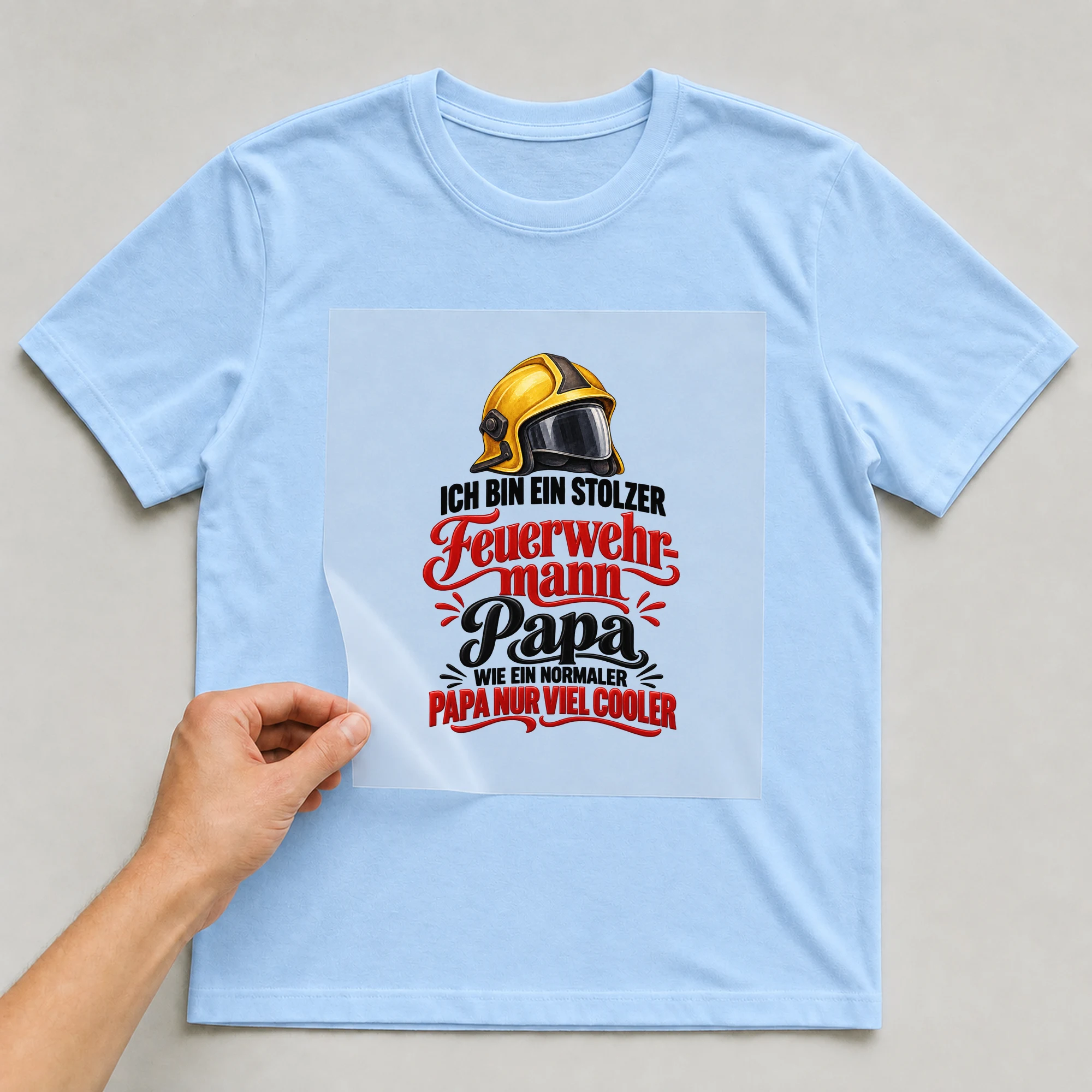 Bügelbild „Ich bin ein stolzer Feuerwehr-Mann Papa wie ein normaler Papa nur viel cooler“ auf babyblauem T-Shirt, Folie wird aufgelegt