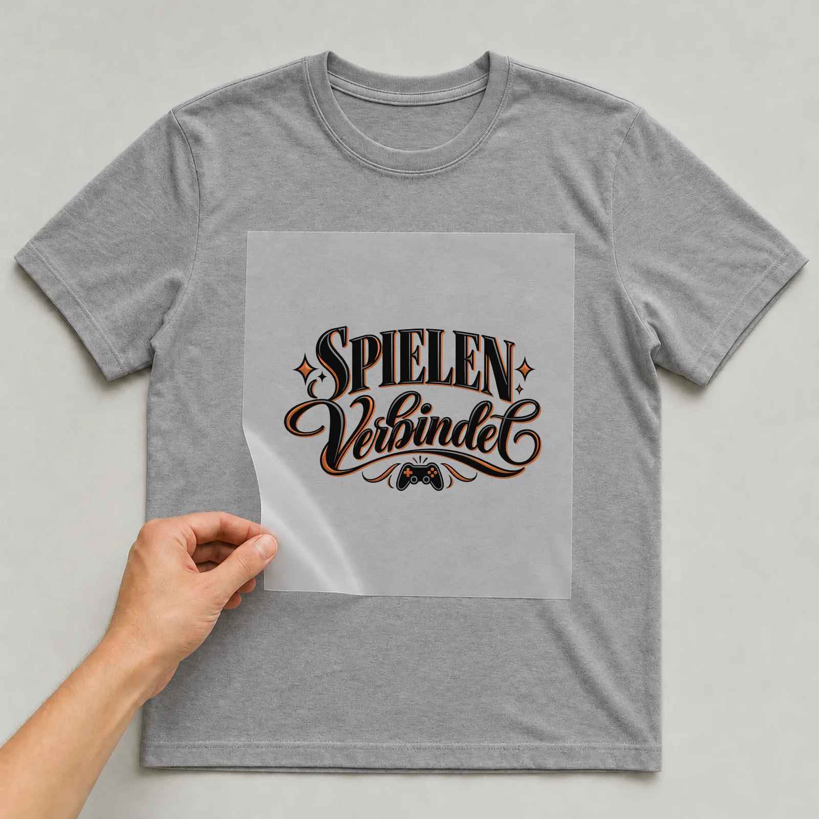 Bügelbild „Spielen verbindet“ auf grauem T-Shirt, Folie wird aufgelegt
