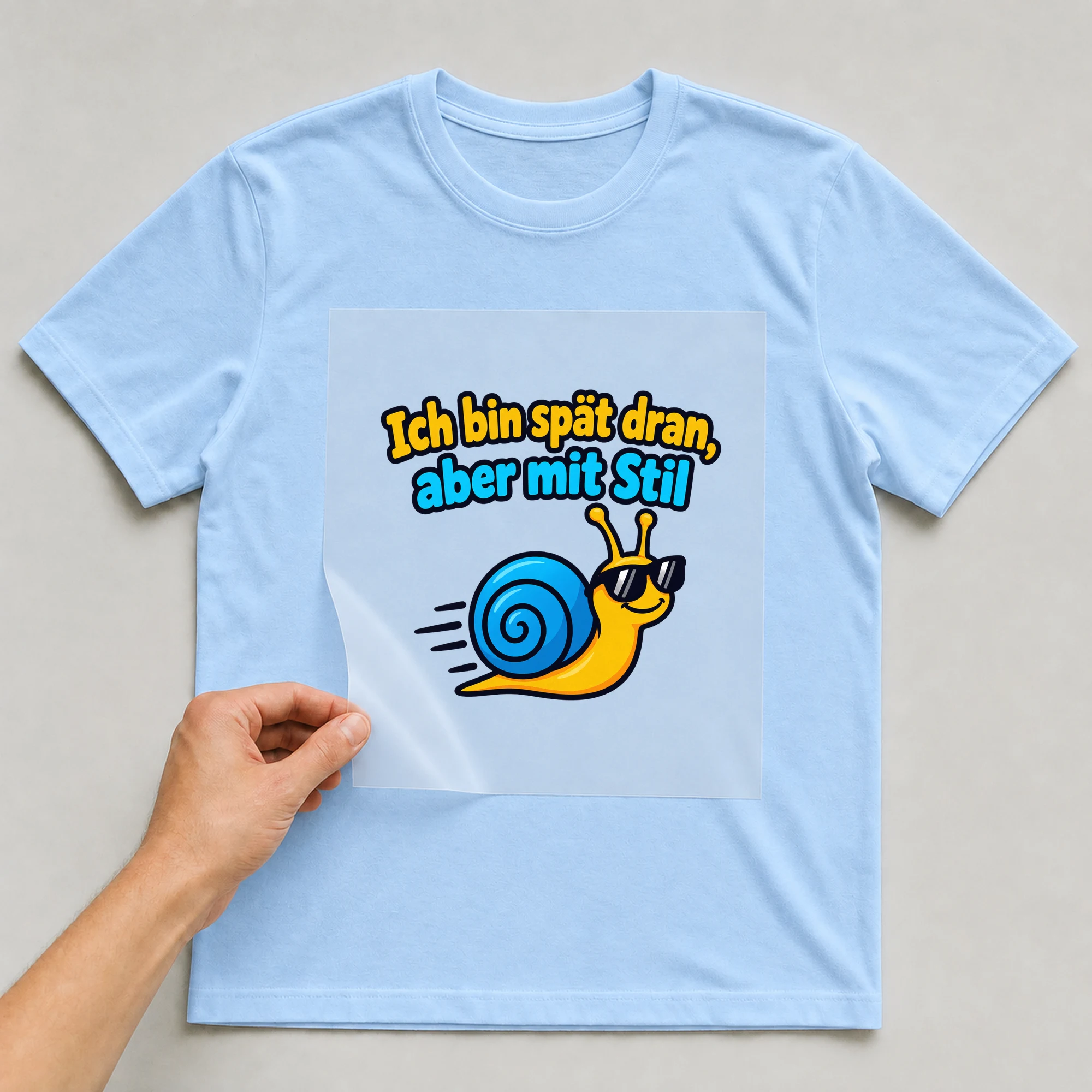 Bügelbild „Ich bin spät dran, aber mit Stil“ auf babyblauem T-Shirt, Folie wird aufgelegt