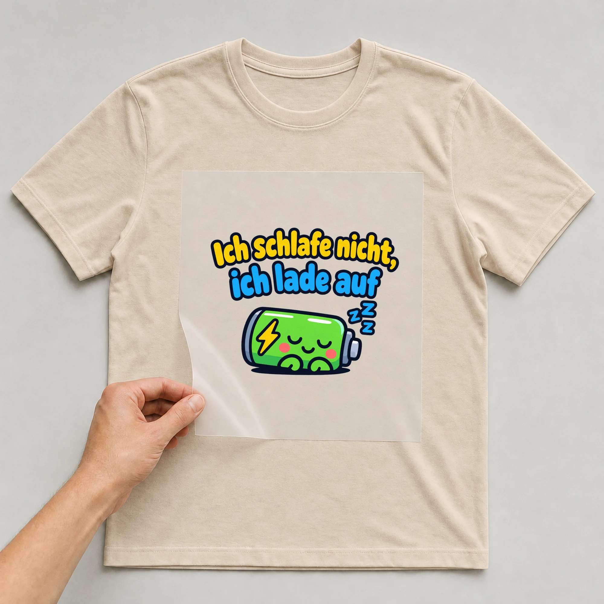 Bügelbild „Ich schlafe nicht, ich lade auf“ auf beigem T-Shirt, Folie wird aufgelegt