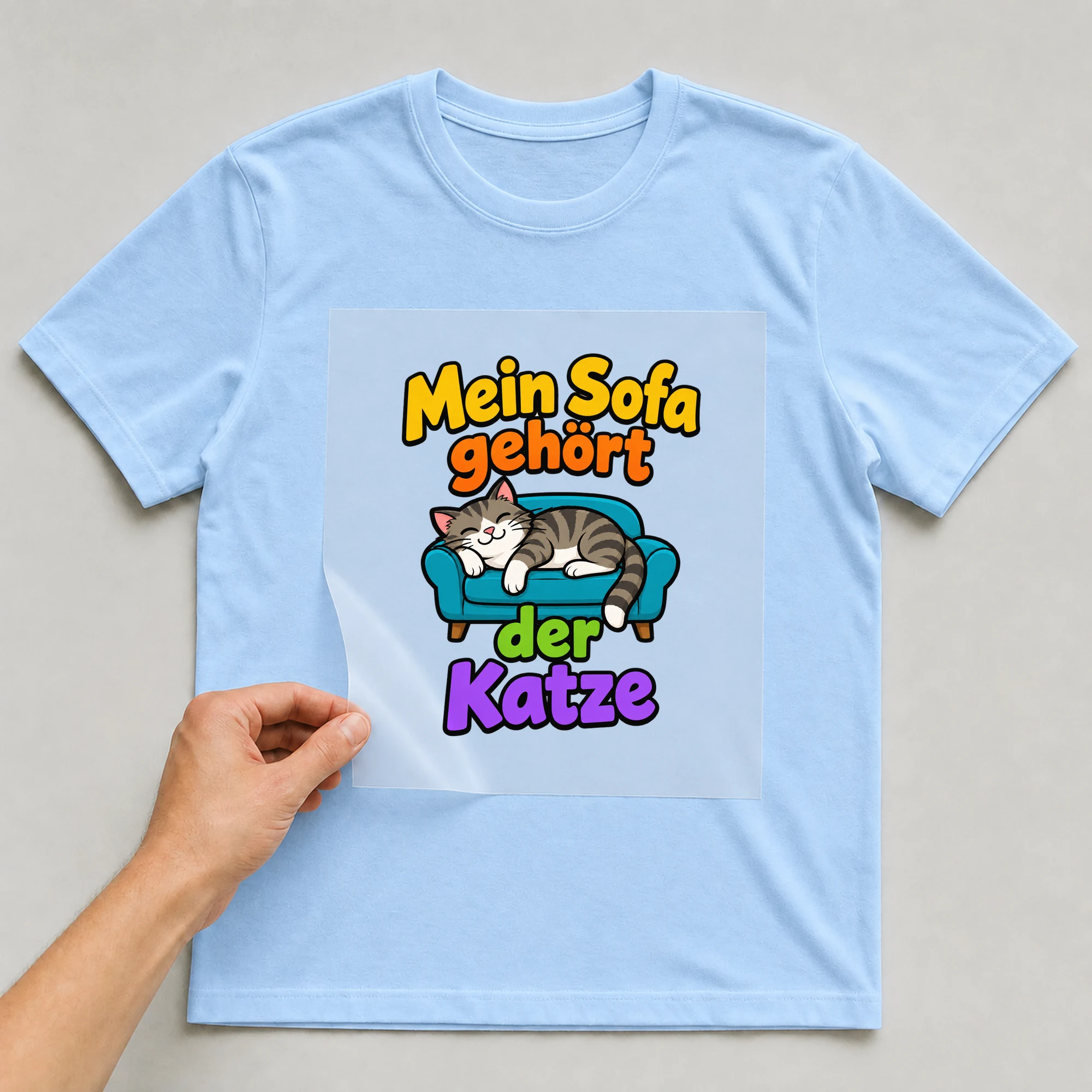 Bügelbild „Mein Sofa gehört der Katze“ auf babyblauem T-Shirt, Folie wird aufgelegt