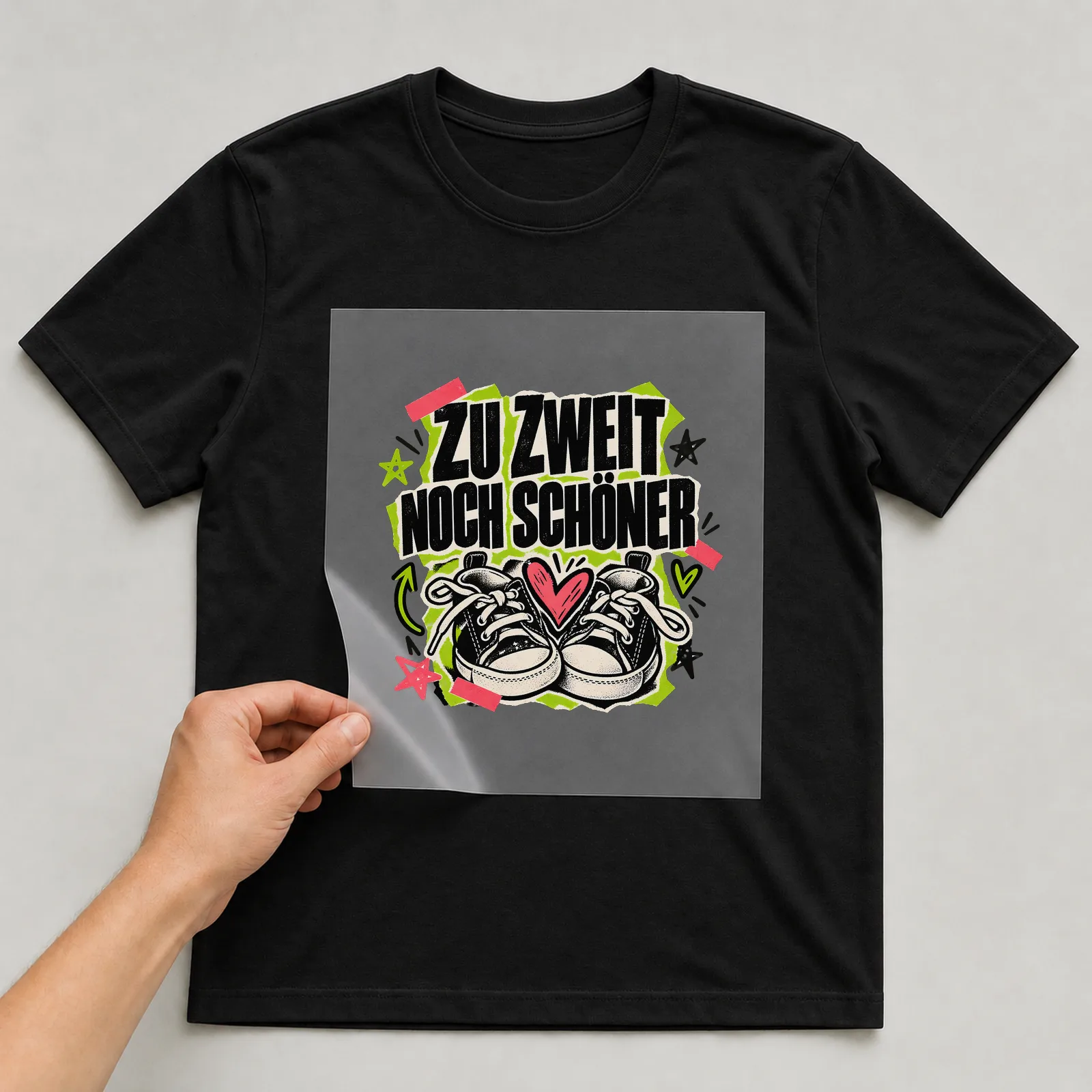 Bügelbild „Zu zweit noch schöner“ auf schwarzem T-Shirt, Folie wird aufgelegt