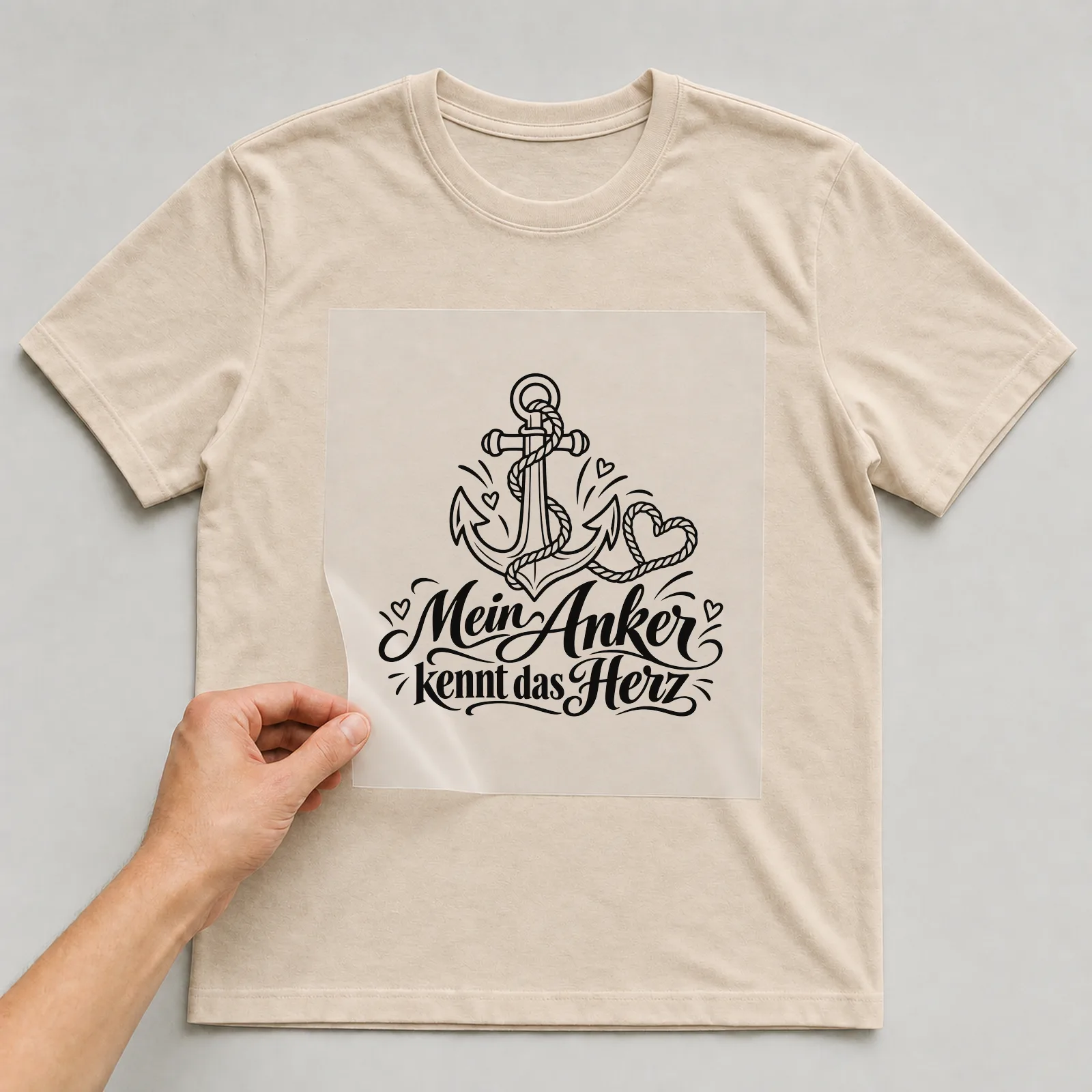 Bügelbild „Mein Anker kennt das Herz“ auf beigem T-Shirt, Folie wird aufgelegt