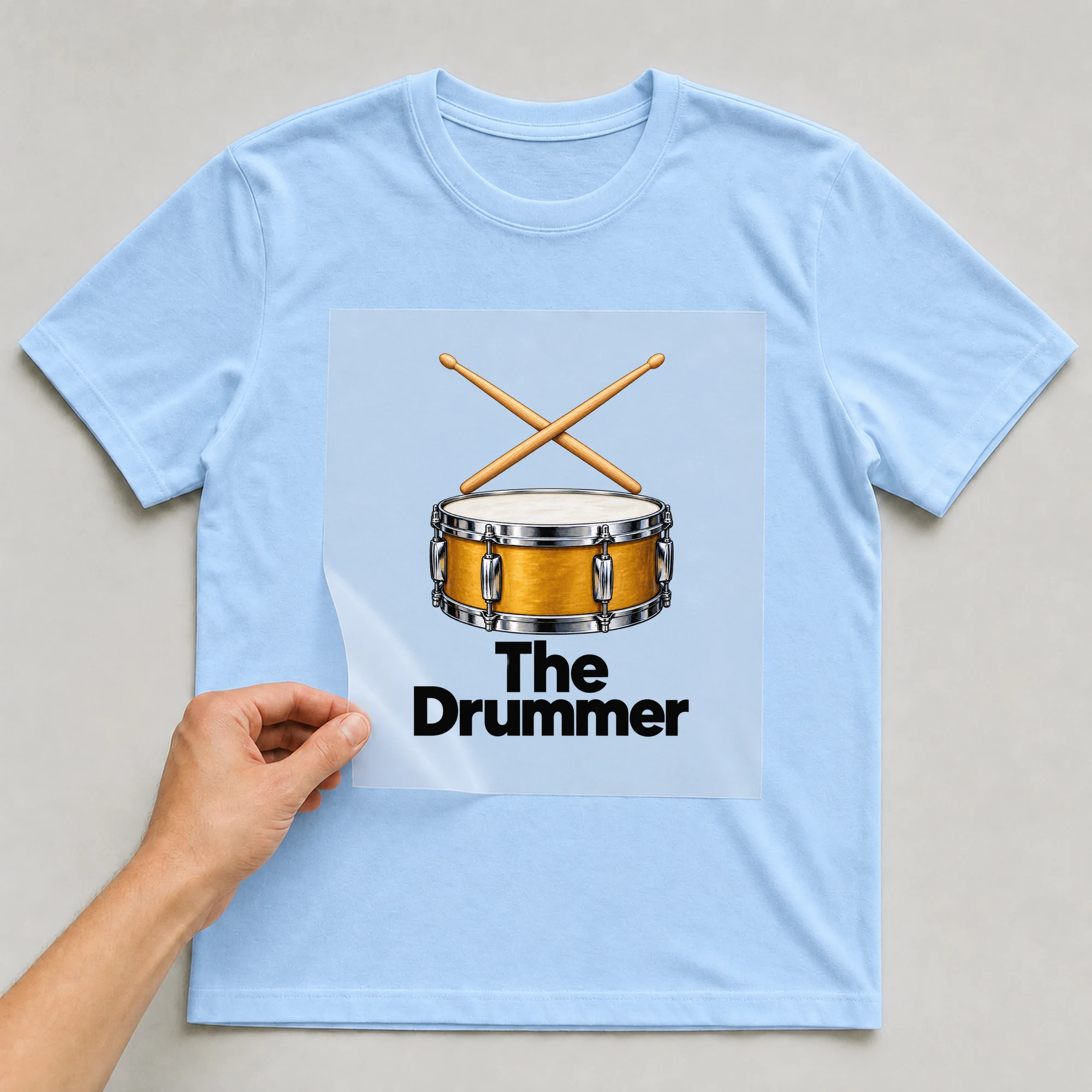 Bügelbild „The Drummer“ auf babyblauem T-Shirt, Folie wird aufgelegt