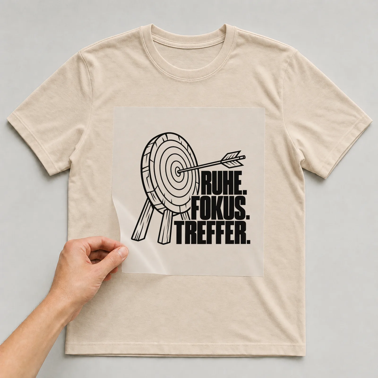 Bügelbild „Ruhe. Fokus. Treffer.“ auf beigem T-Shirt, Folie wird aufgelegt