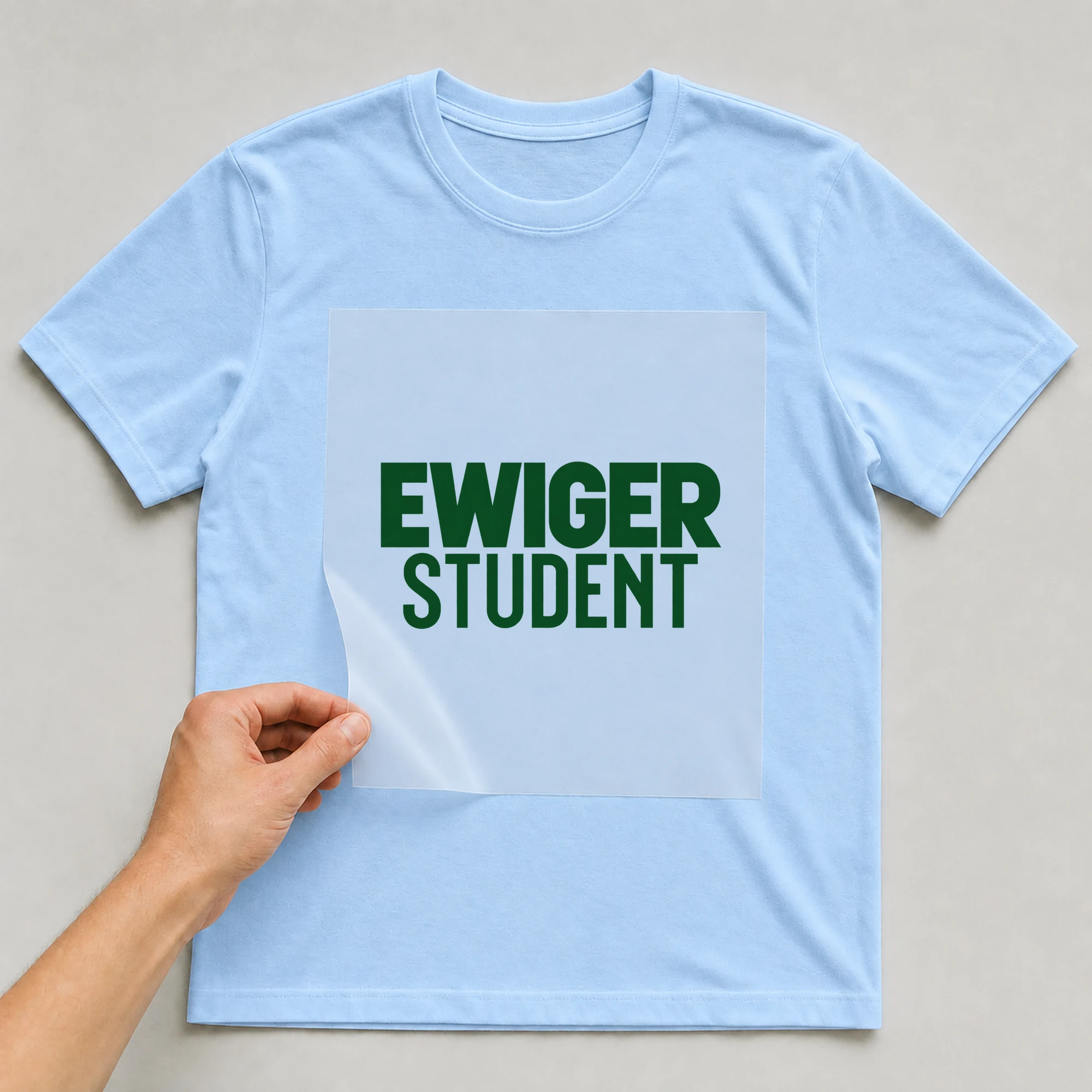 Bügelbild „Ewiger Student“ auf babyblauem T-Shirt, Folie wird aufgelegt
