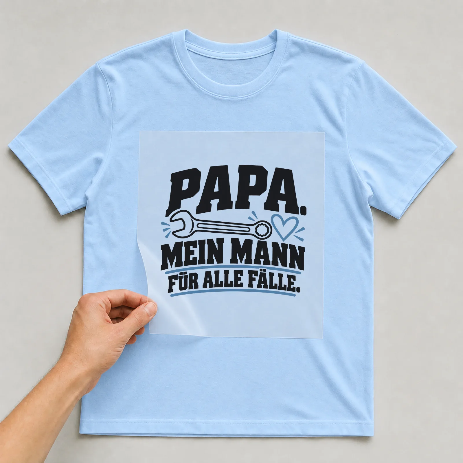 Bügelbild „Papa. Mein Mann für alle fälle.“ auf hellblauem T-Shirt, Folie wird aufgelegt