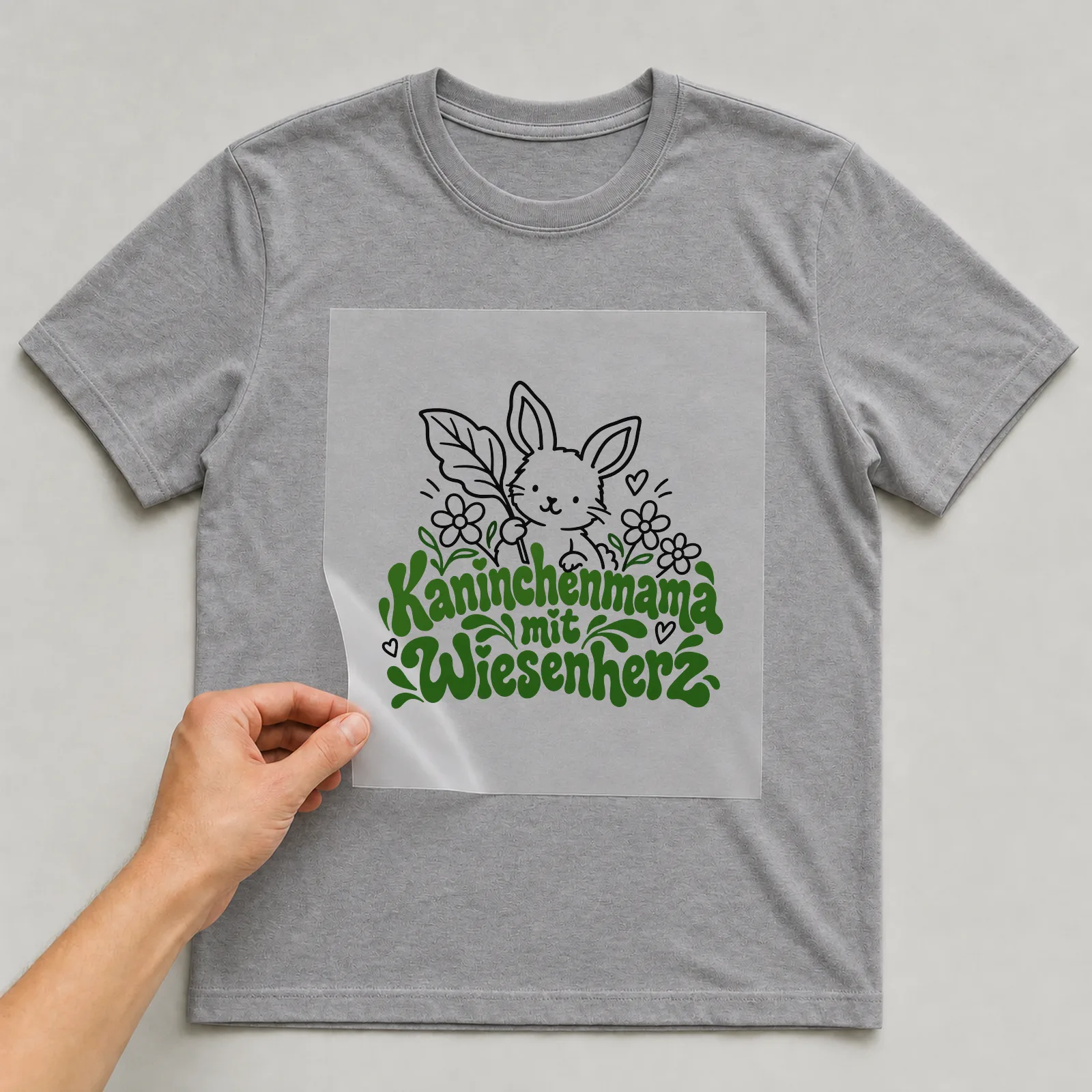 Bügelbild „Kaninchenmama mit Wiesenherz“ auf grauem T-Shirt, Folie wird aufgelegt