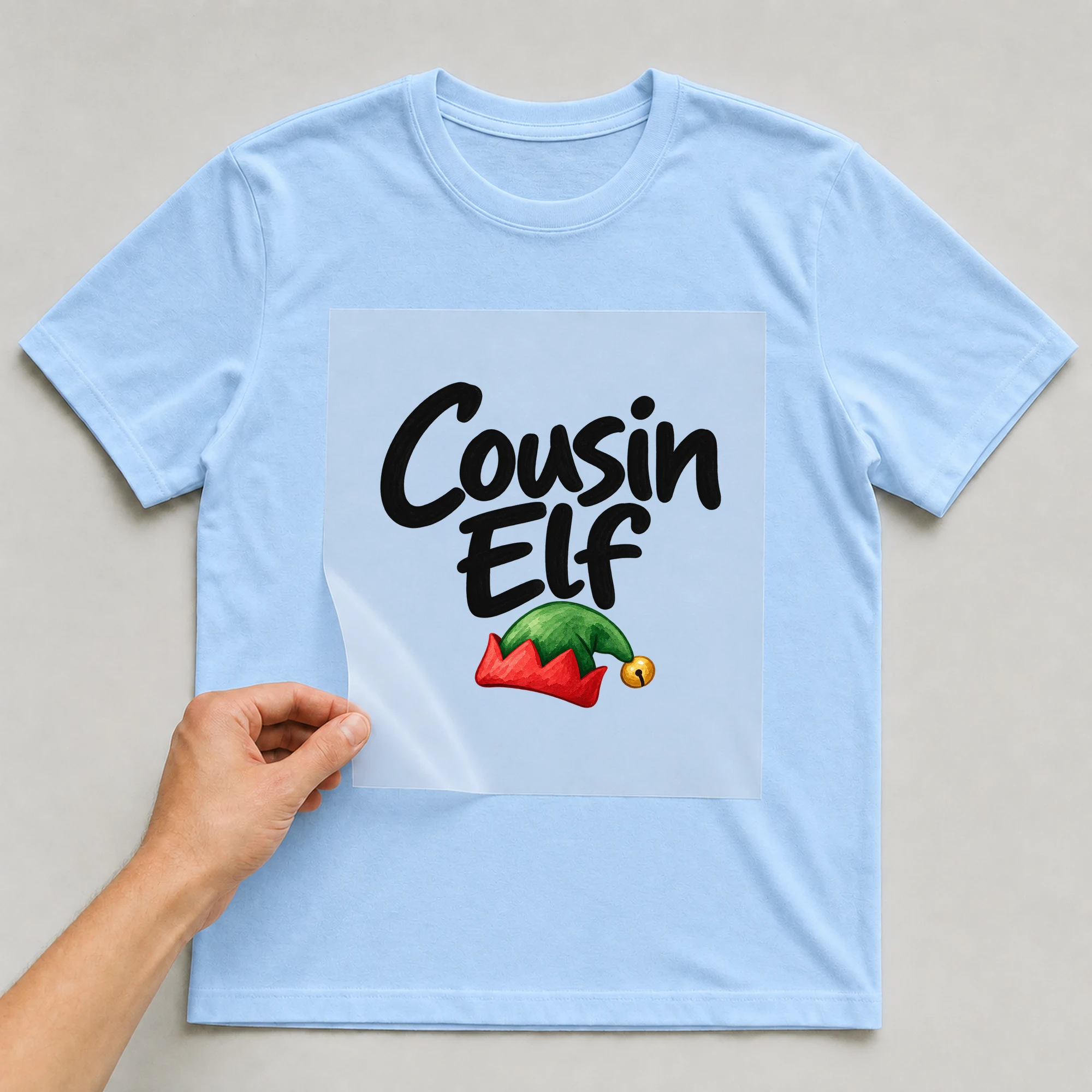 Bügelbild „Cousin Elf“ auf babyblauem T-Shirt, Folie wird aufgelegt