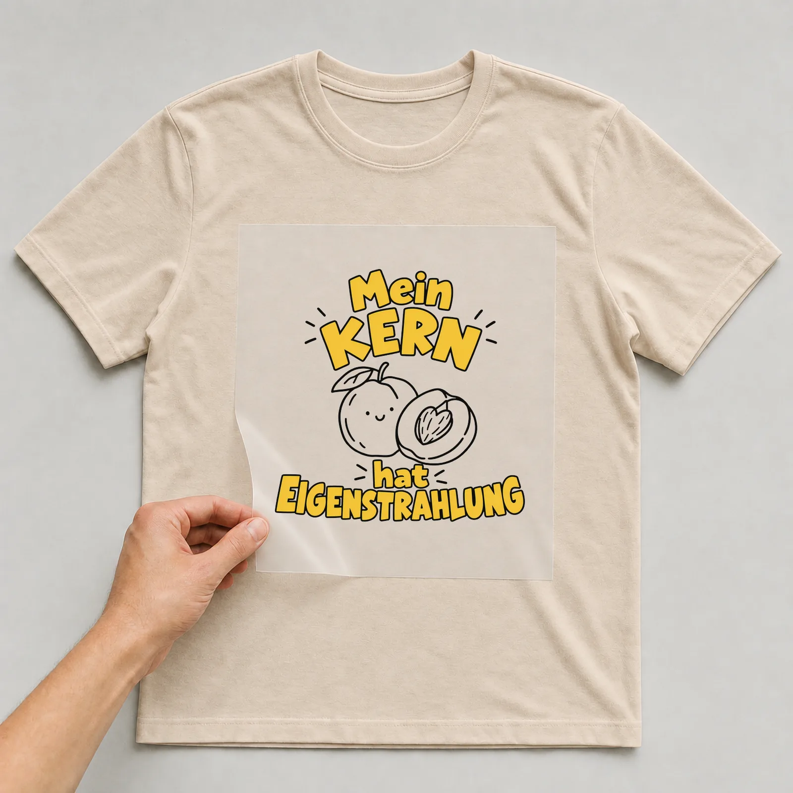 Bügelbild „Mein Kern hat Eigenstrahlung“ auf beigem T-Shirt, Folie wird aufgelegt