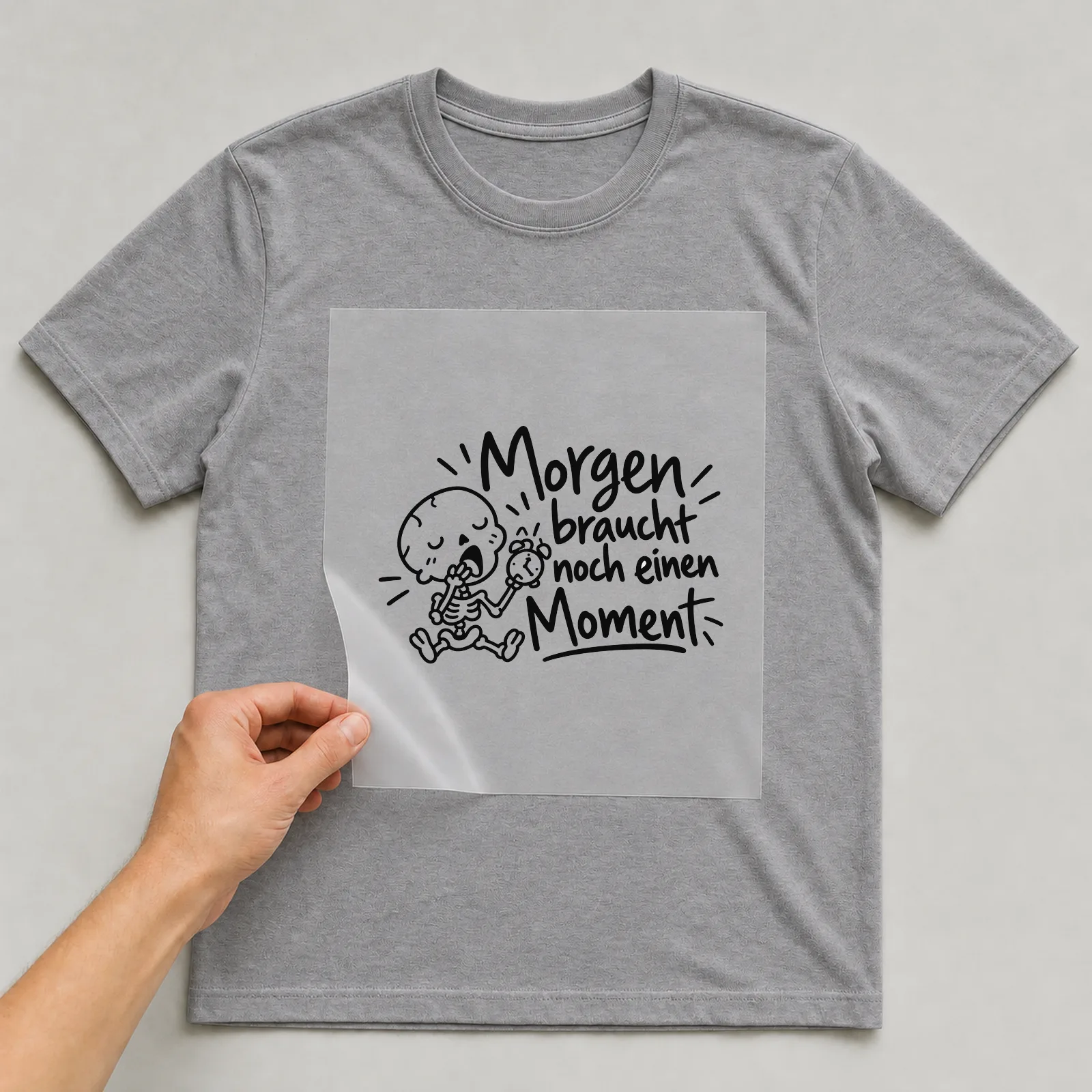 Bügelbild „Morgen braucht noch einen Moment“ auf grauem T-Shirt, Folie wird aufgelegt