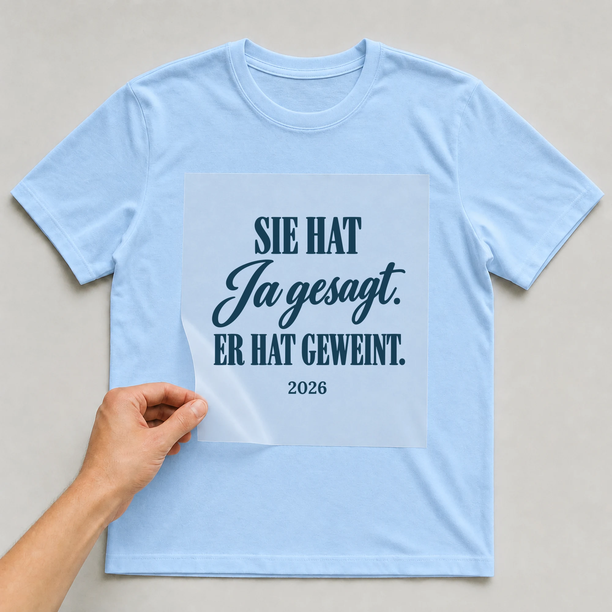 Bügelbild Sie hat Ja gesagt. Er hat geweint mit Jahr auf hellblauem T-Shirt, Folie wird aufgelegt