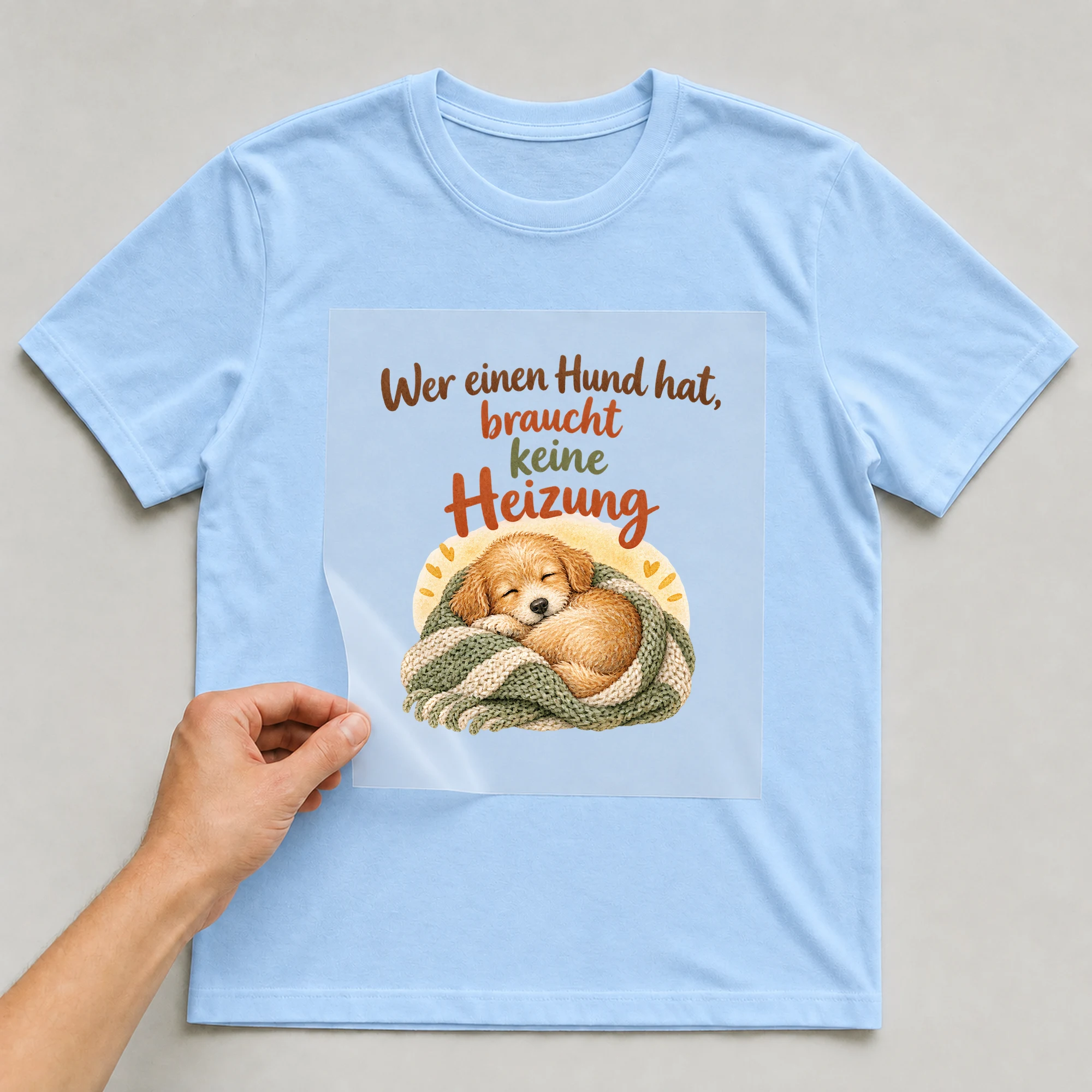 Bügelbild „Wer einen Hund hat, braucht keine Heizung“ auf babyblauem T-Shirt, Folie wird aufgelegt