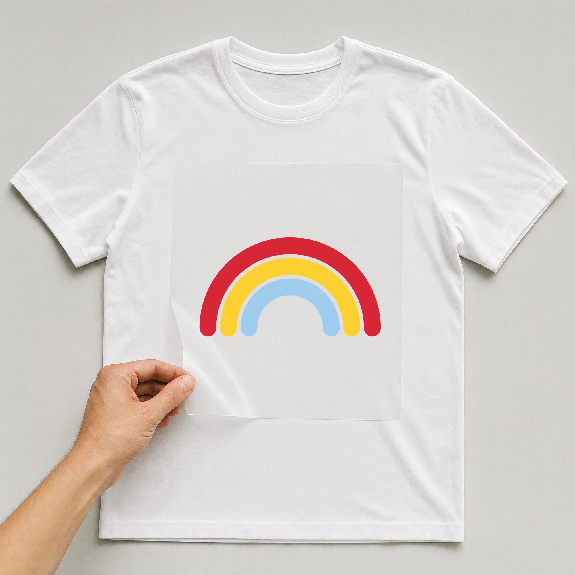 Bügelbild „Regenbogen“ auf weißem T-Shirt, Folie wird aufgelegt