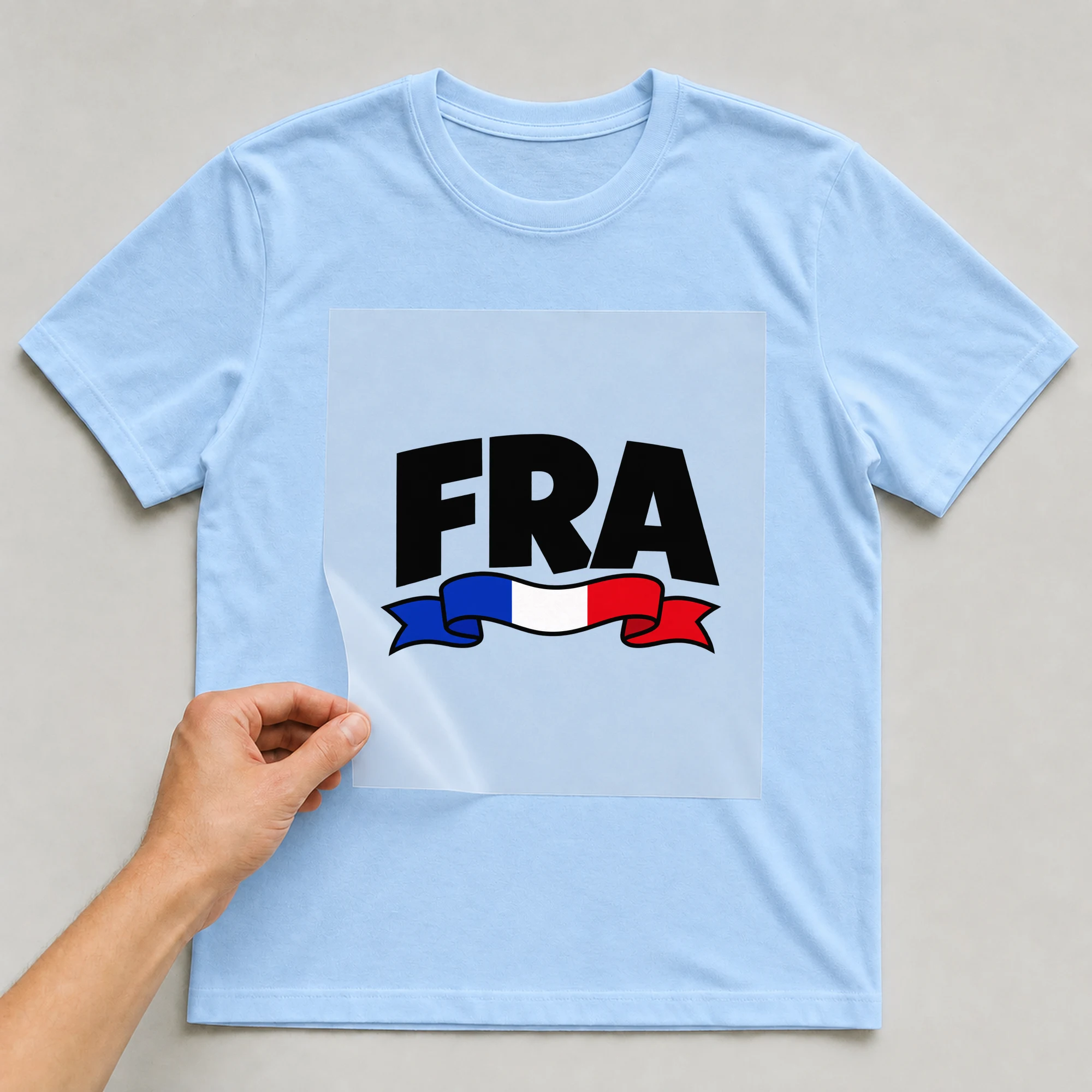 Bügelbild „FRA“ auf babyblauem T-Shirt, Folie wird aufgelegt