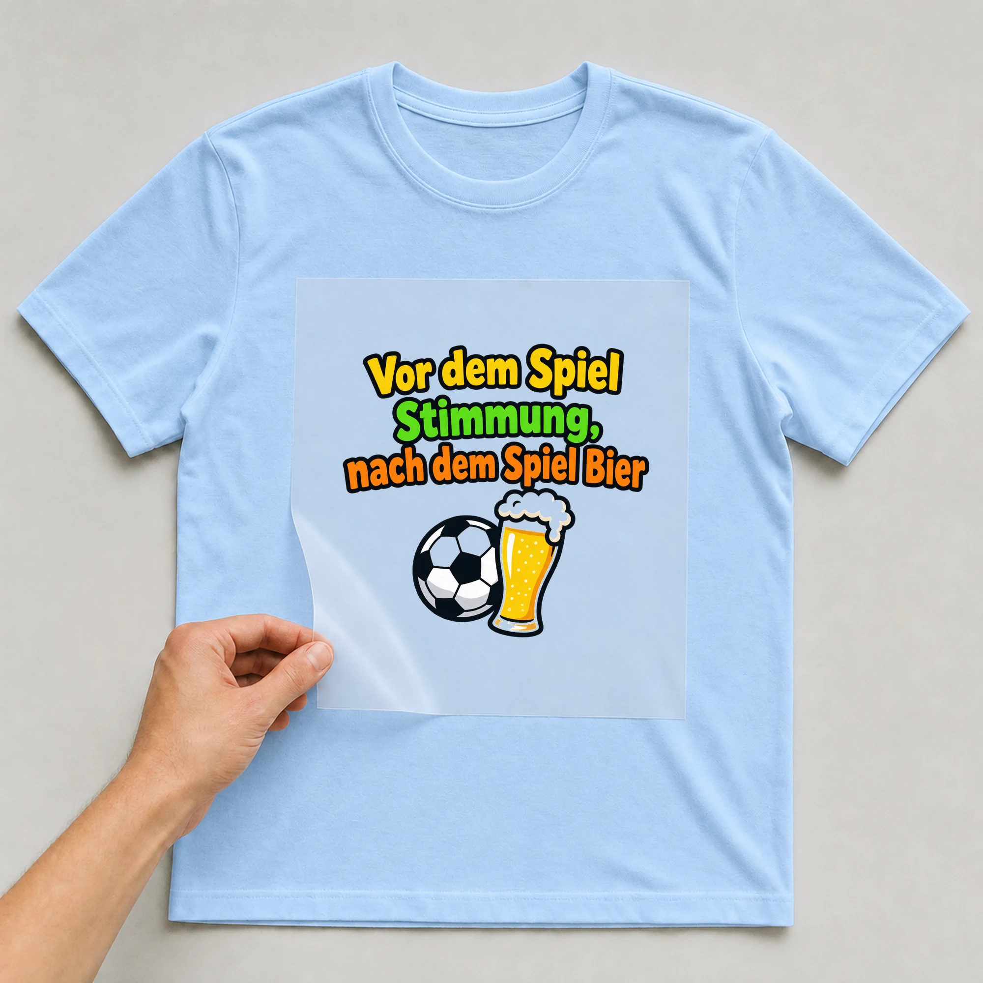 Bügelbild „Vor dem Spiel Stimmung, nach dem Spiel Bier“ auf babyblauem T-Shirt, Folie wird aufgelegt