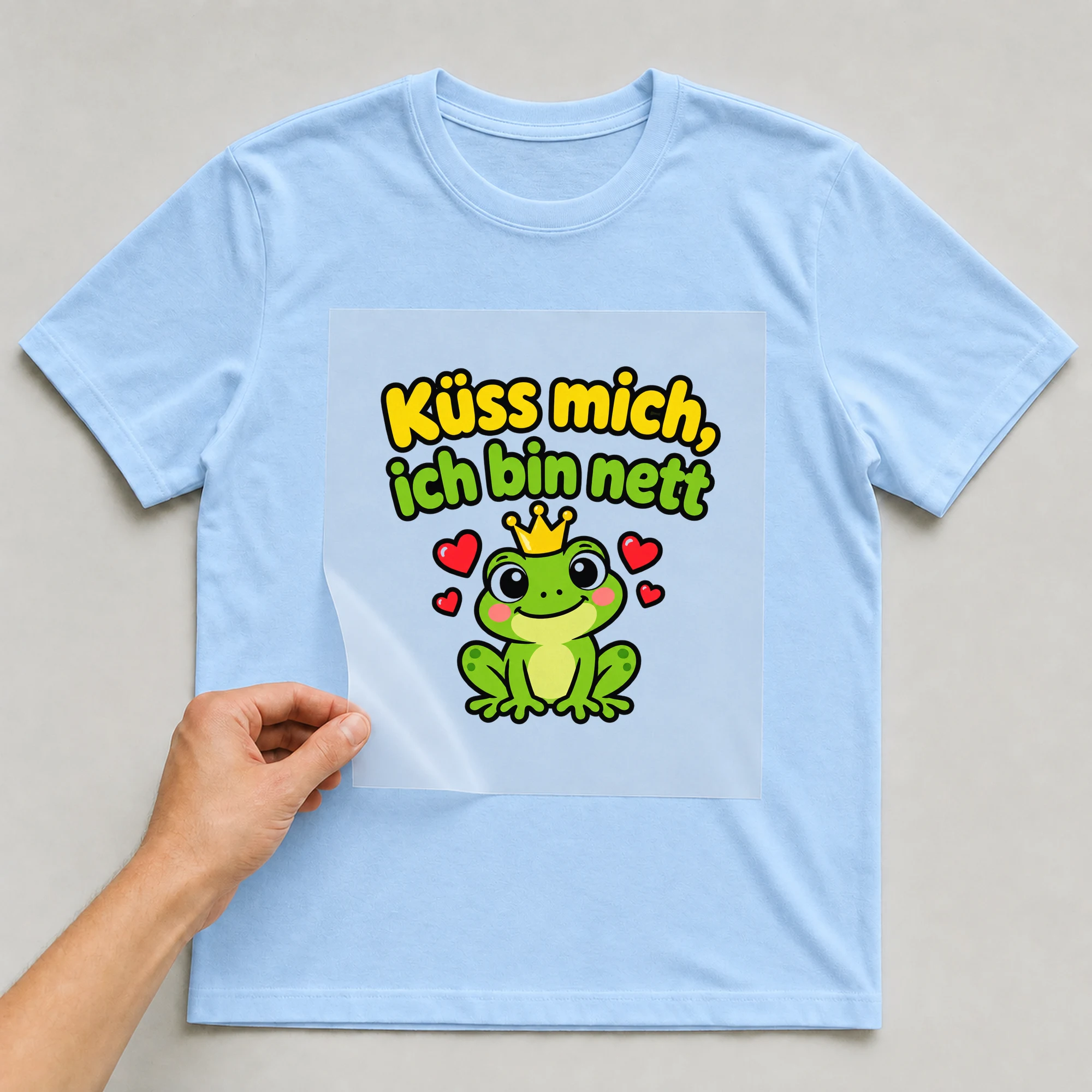 Bügelbild „Küss mich, ich bin nett“ auf babyblauem T-Shirt, Folie wird aufgelegt