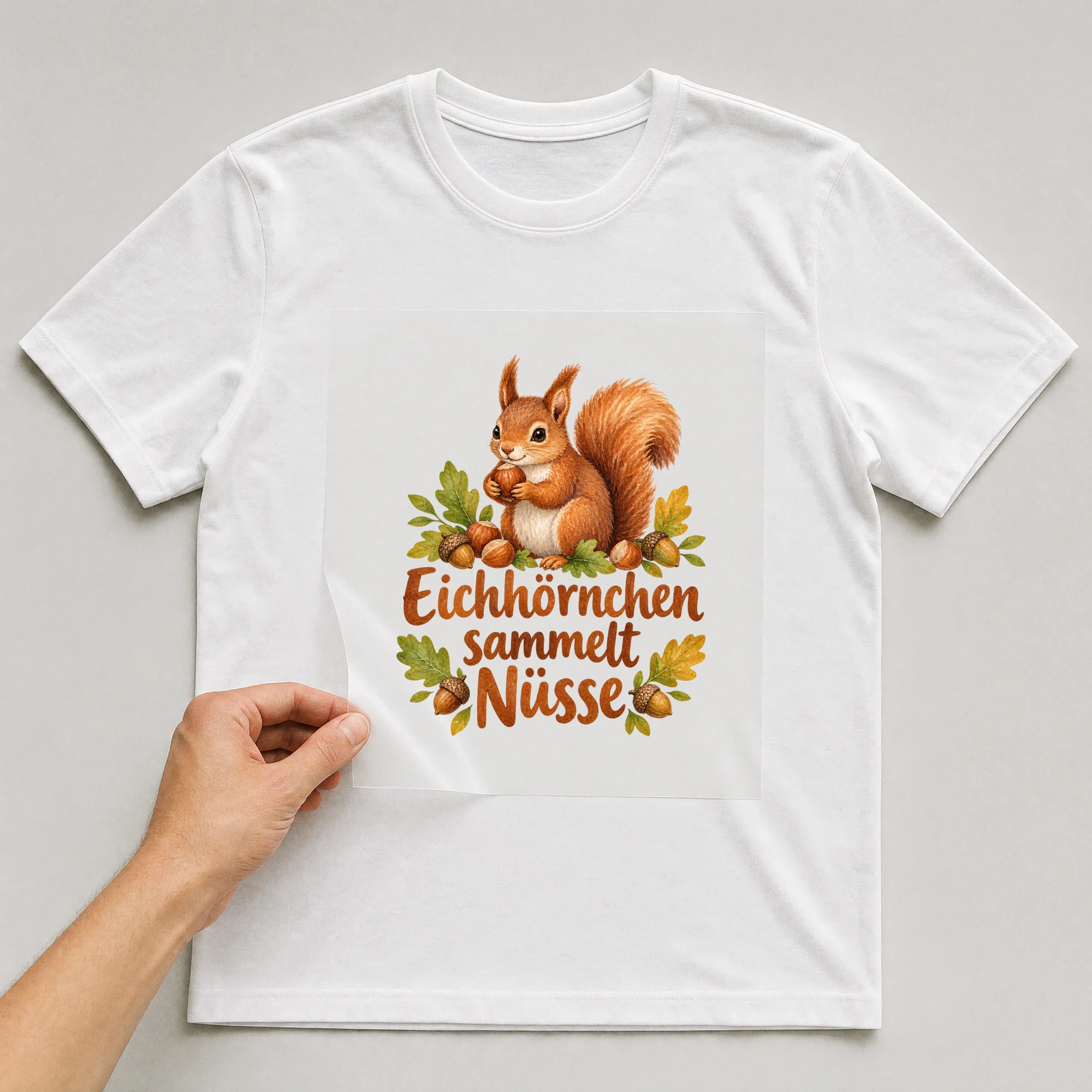 Bügelbild „Eichhörnchen sammelt Nüsse“ auf weißem T-Shirt, Folie wird aufgelegt