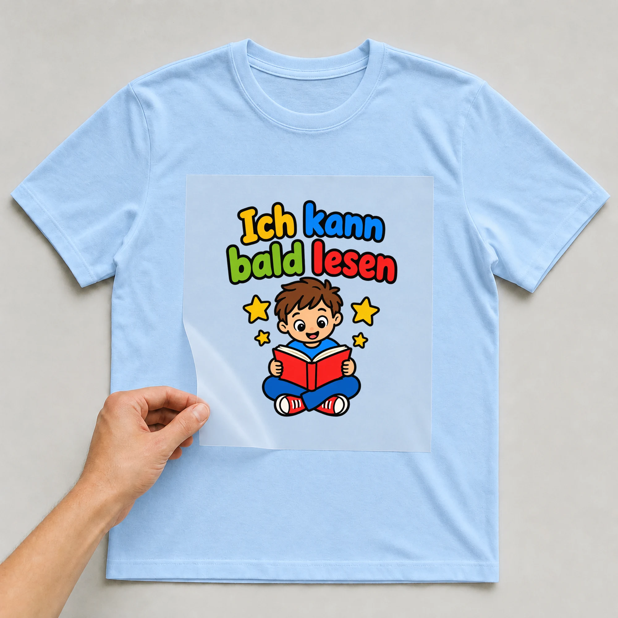 Bügelbild „Ich kann bald lesen“ auf babyblauem T-Shirt, Folie wird aufgelegt