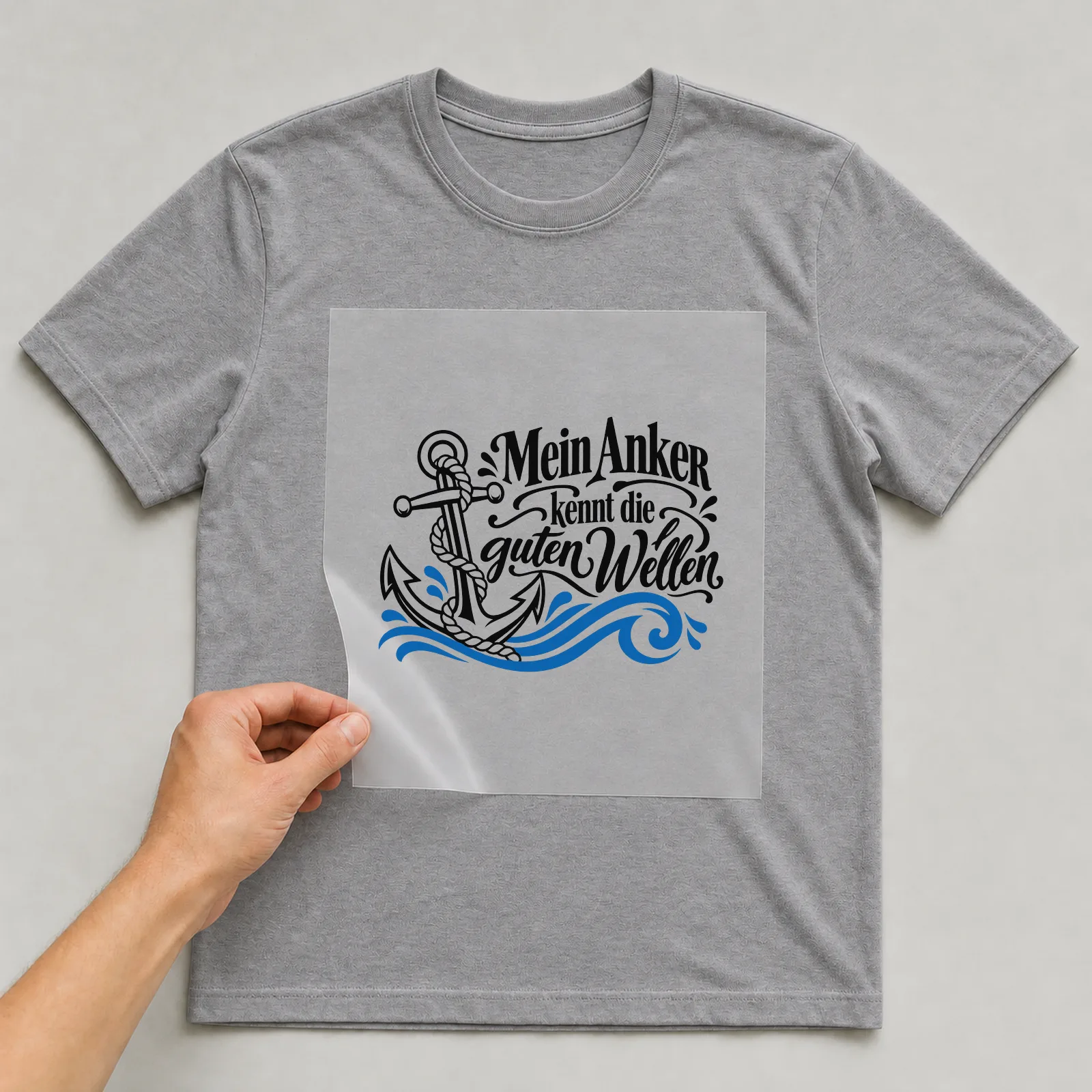 Bügelbild „Mein Anker kennt die guten Wellen“ auf grauem T-Shirt, Folie wird aufgelegt