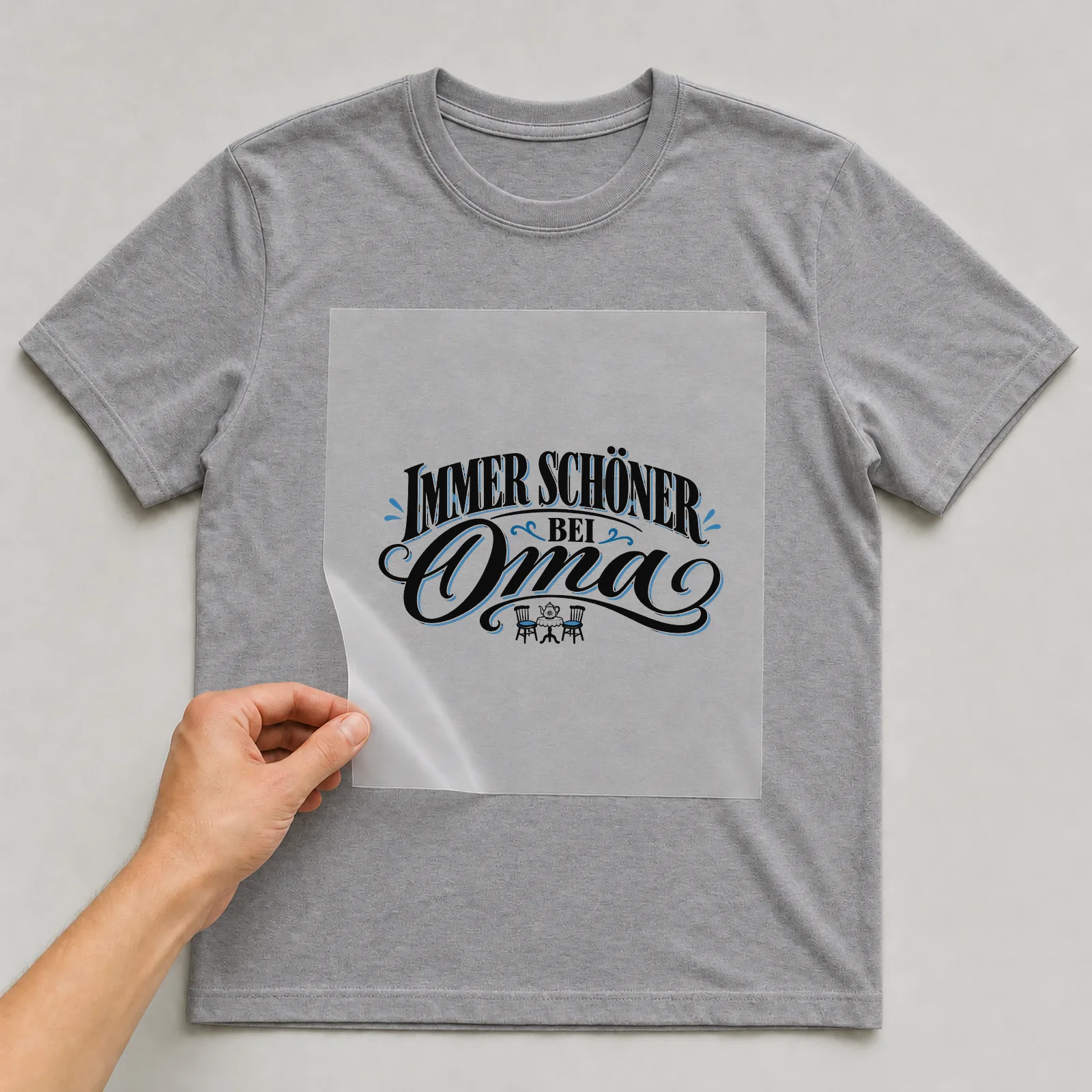 Bügelbild „Immer schöner bei Oma“ auf grauem T-Shirt, Folie wird aufgelegt