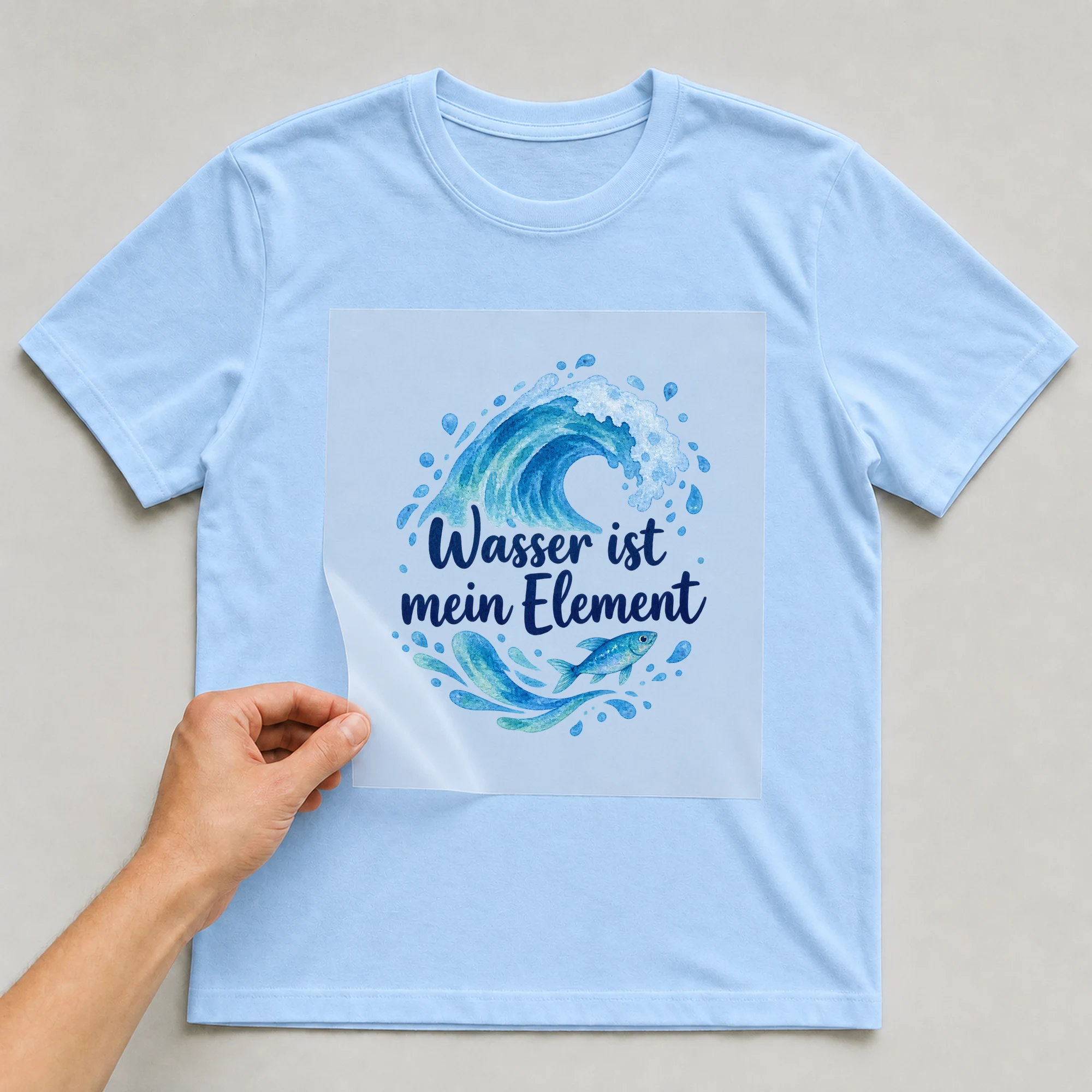 Bügelbild „Wasser ist mein Element“ auf babyblauem T-Shirt, Folie wird aufgelegt