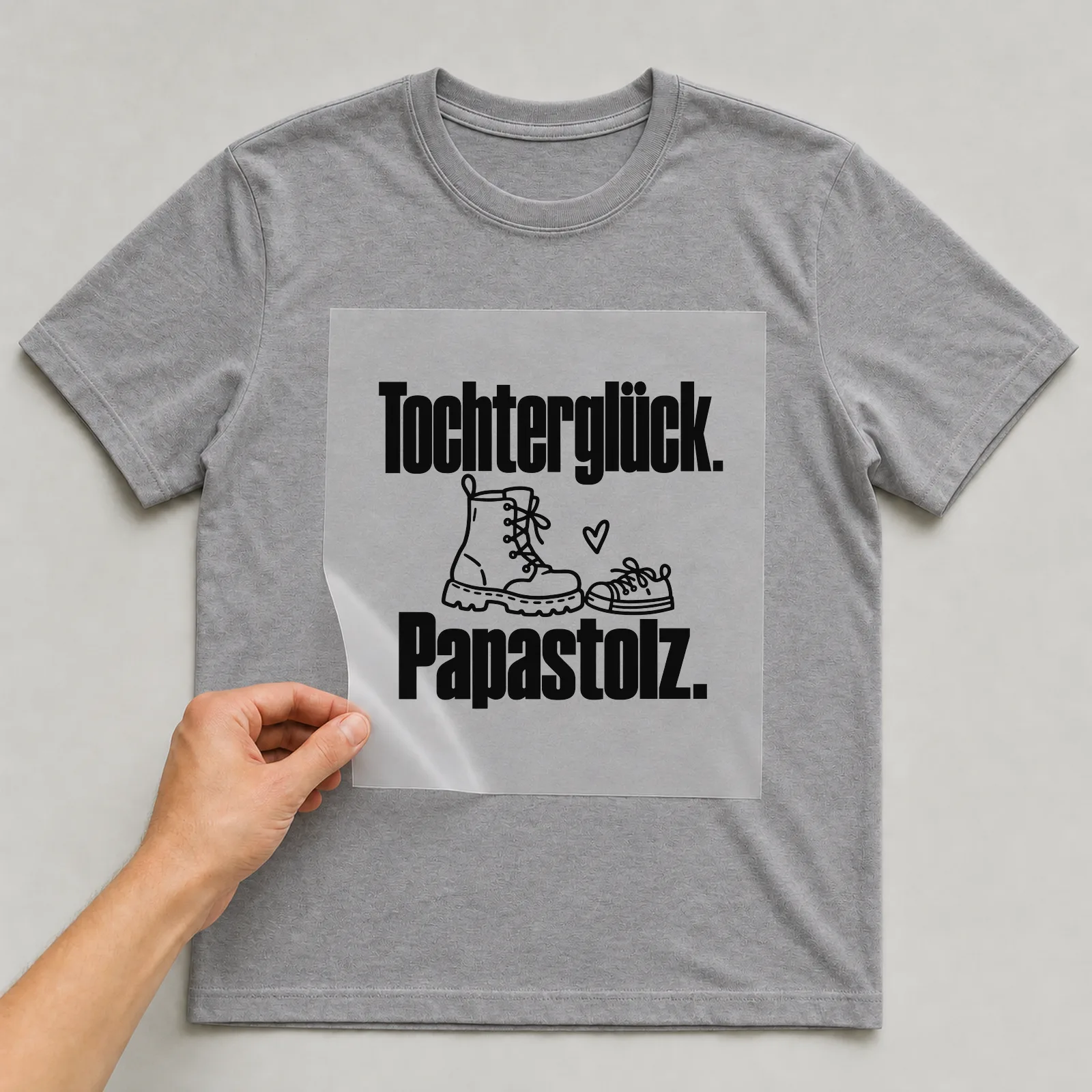 Bügelbild „Tochterglück. Papastolz.“ auf grauem T-Shirt, Folie wird aufgelegt