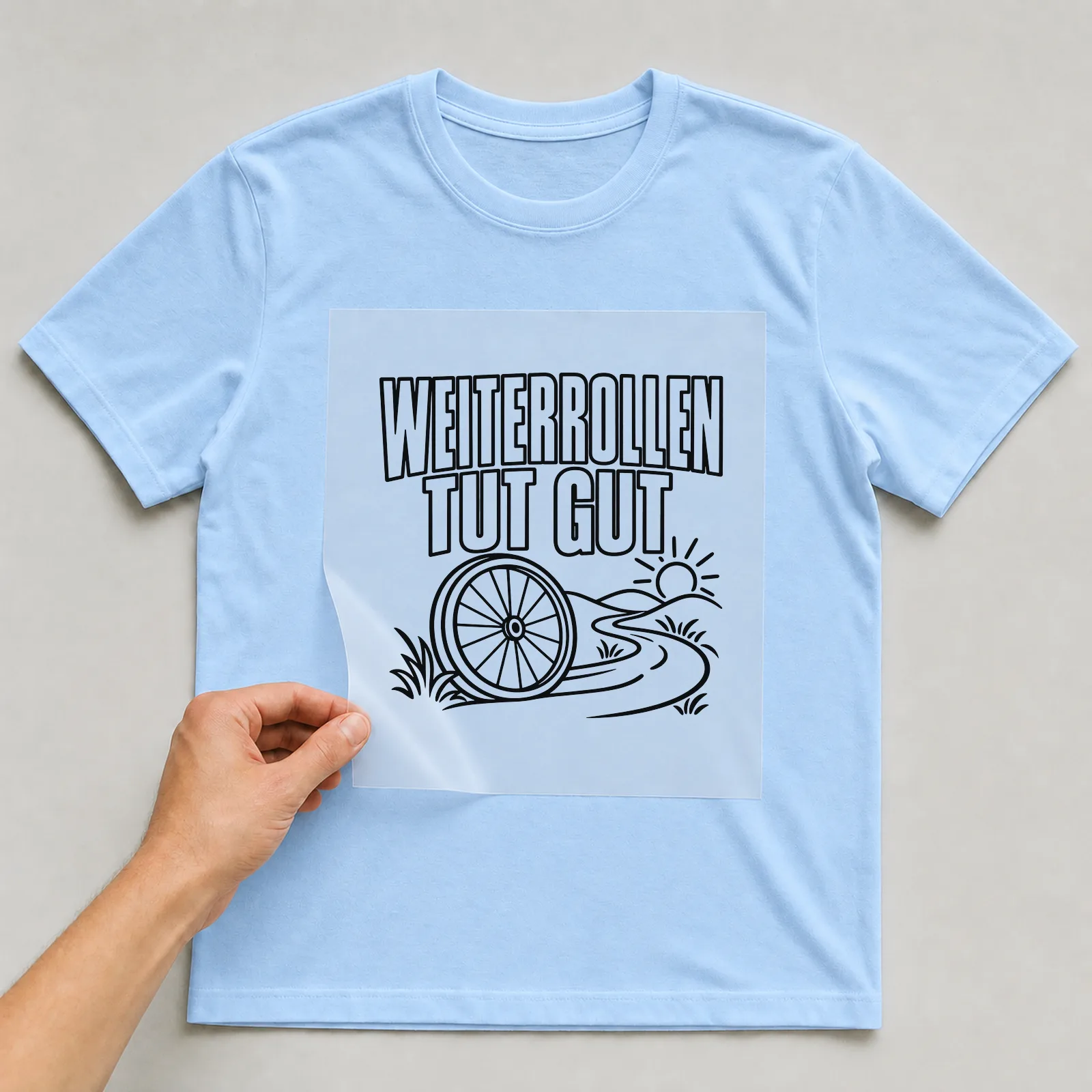 Bügelbild „Weiterrollen tut gut“ auf hellblauem T-Shirt, Folie wird aufgelegt
