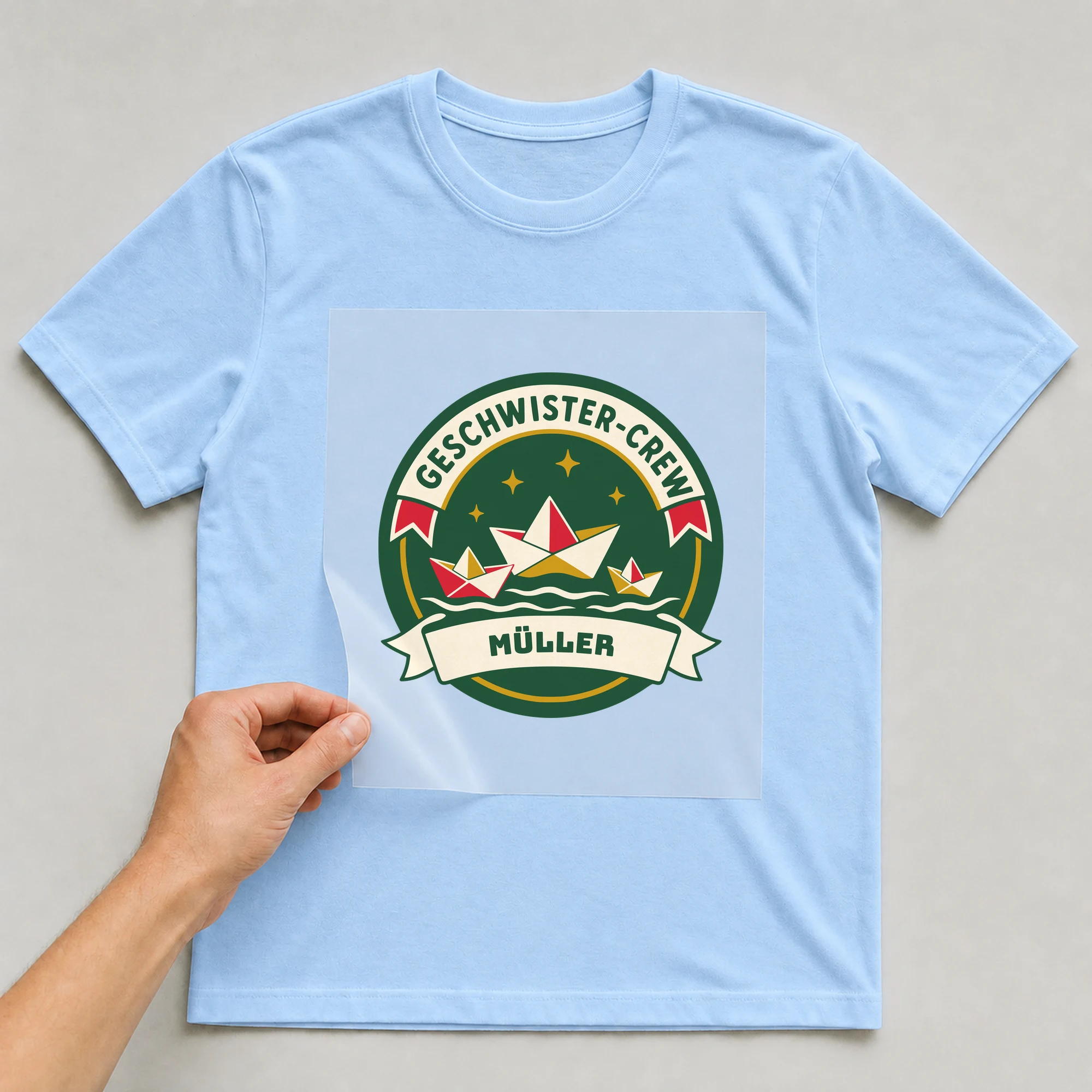 Bügelbild Geschwister-Crew mit Nachname auf hellblauem T-Shirt, Folie wird aufgelegt
