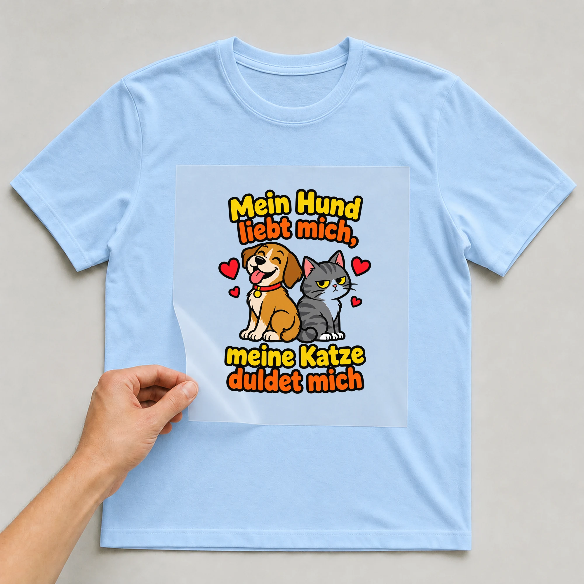 Bügelbild „Mein Hund liebt mich, meine Katze duldet mich“ auf babyblauem T-Shirt, Folie wird aufgelegt