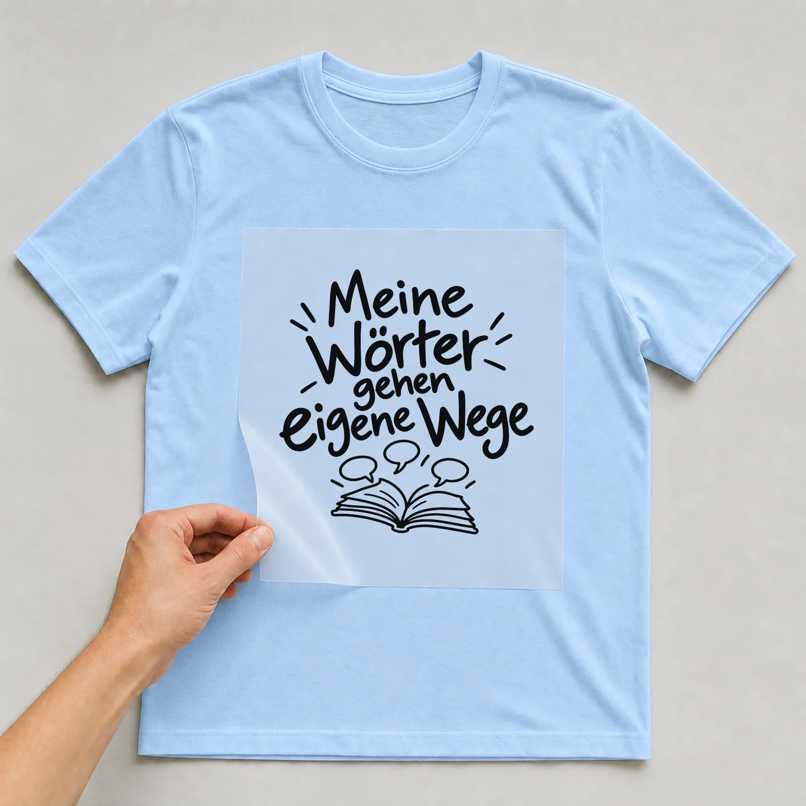 Bügelbild „Meine Wörter gehen eigene Wege“ auf hellblauem T-Shirt, Folie wird aufgelegt