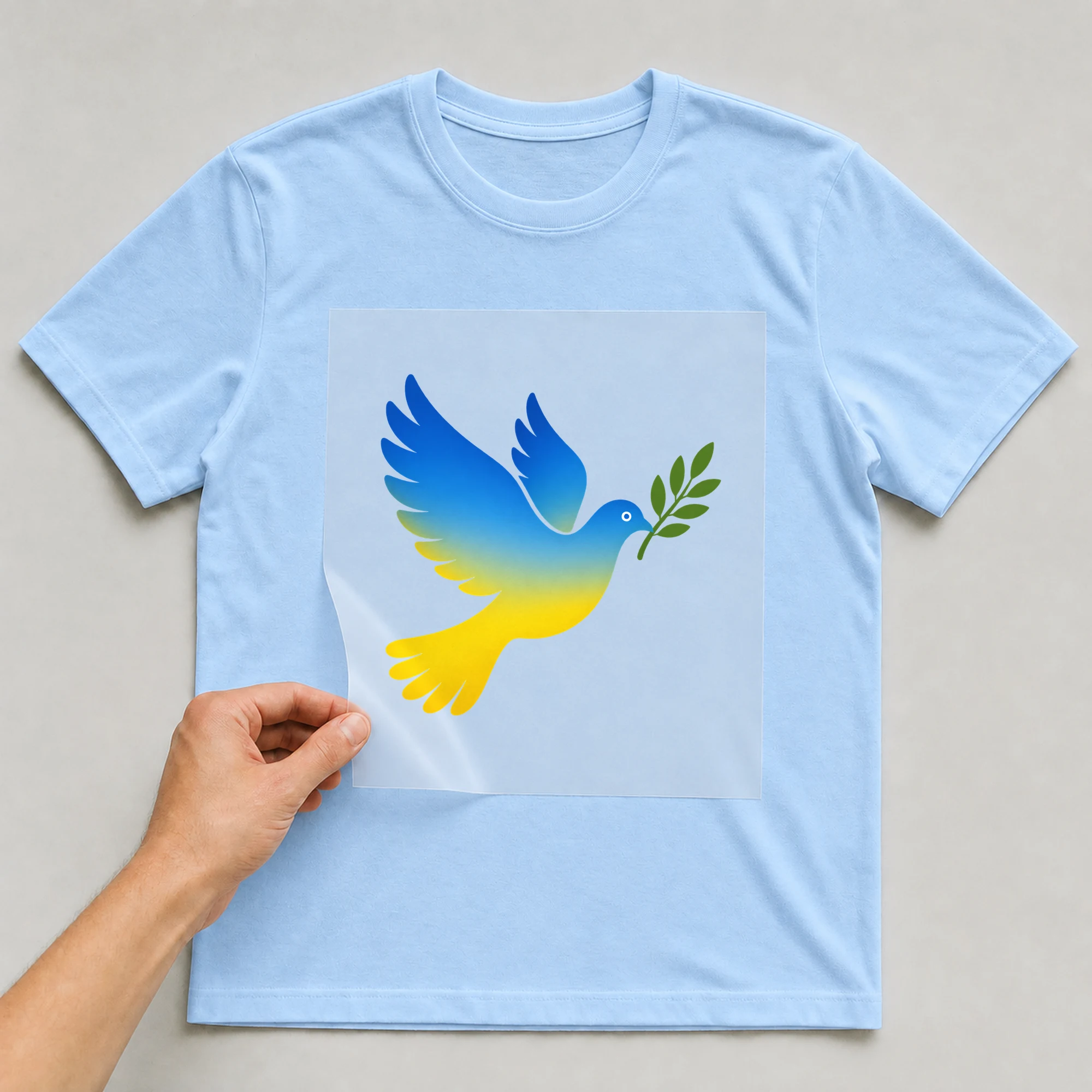 Bügelbild „Friedenstaube blau-gelb“ auf babyblauem T-Shirt, Folie wird aufgelegt