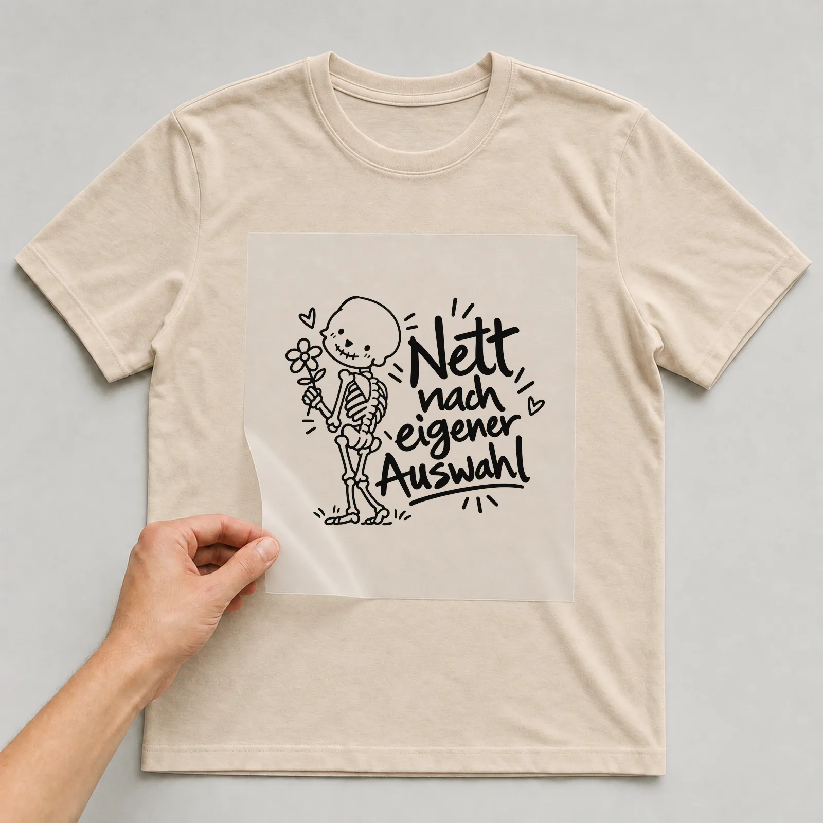 Bügelbild „Nett nach eigener Auswahl“ auf beigem T-Shirt, Folie wird aufgelegt